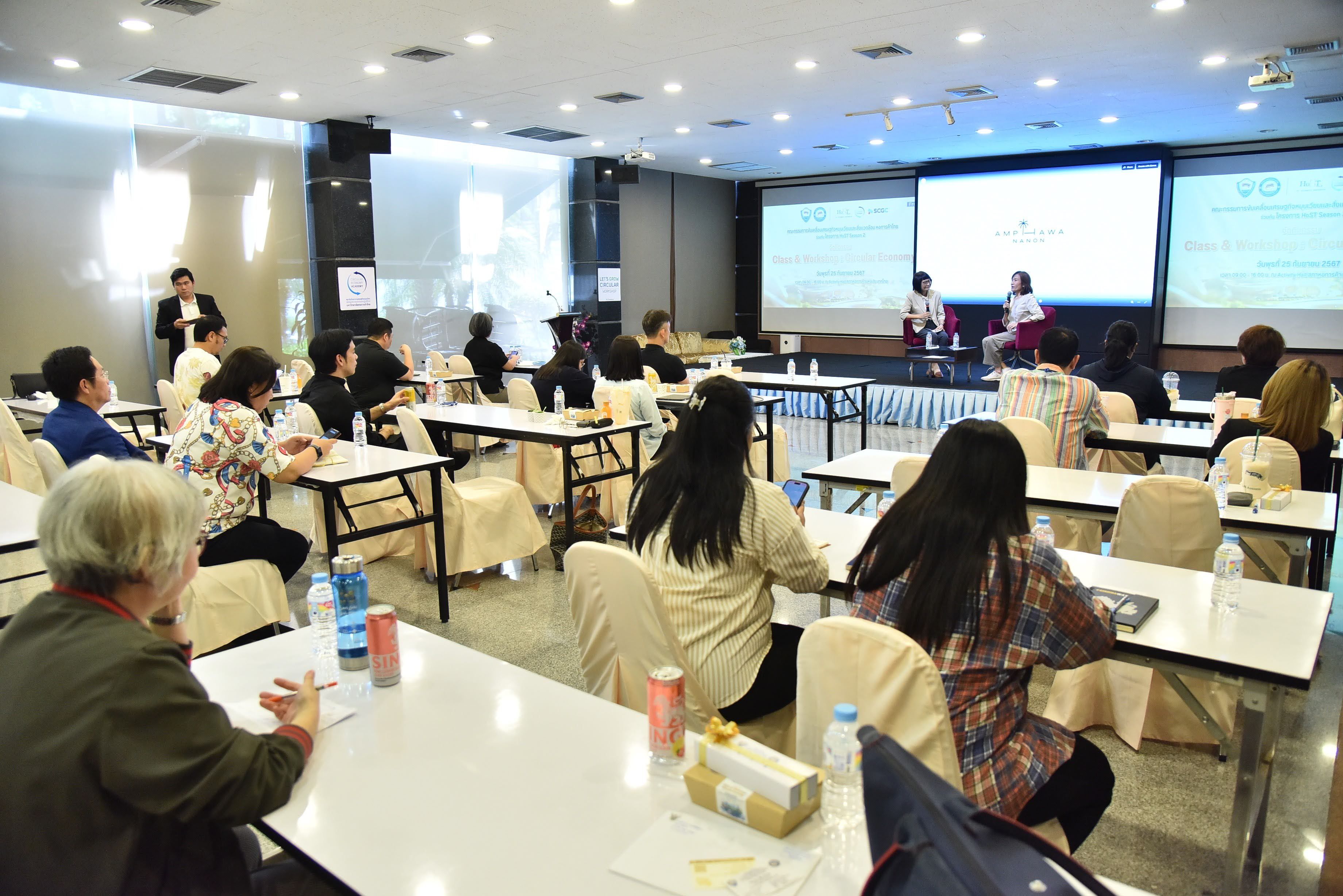 Audience members seated at tables attending a conference with speakers on stage.