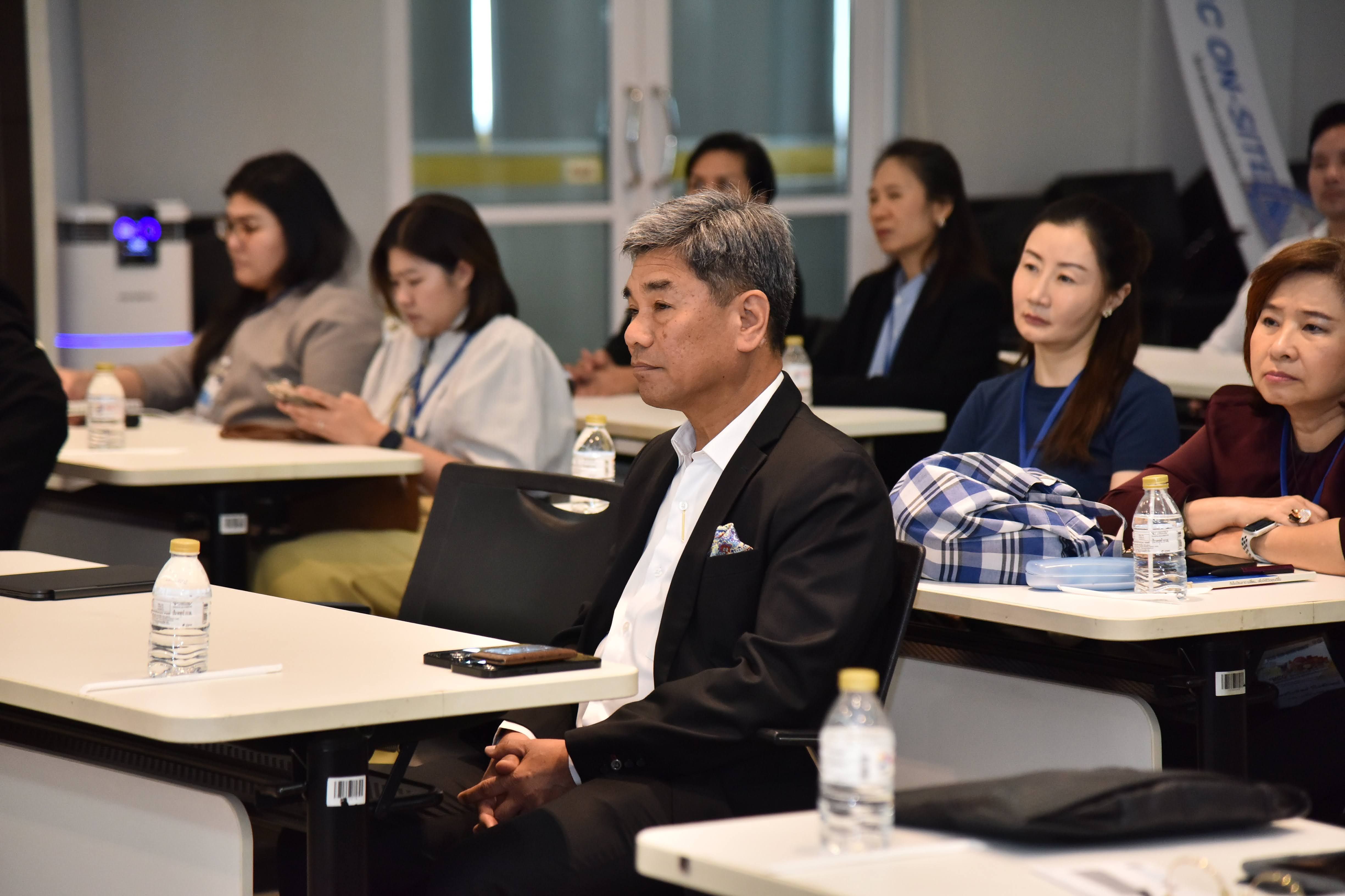 Man in a suit listening intently among seated attendees at a professional conference.