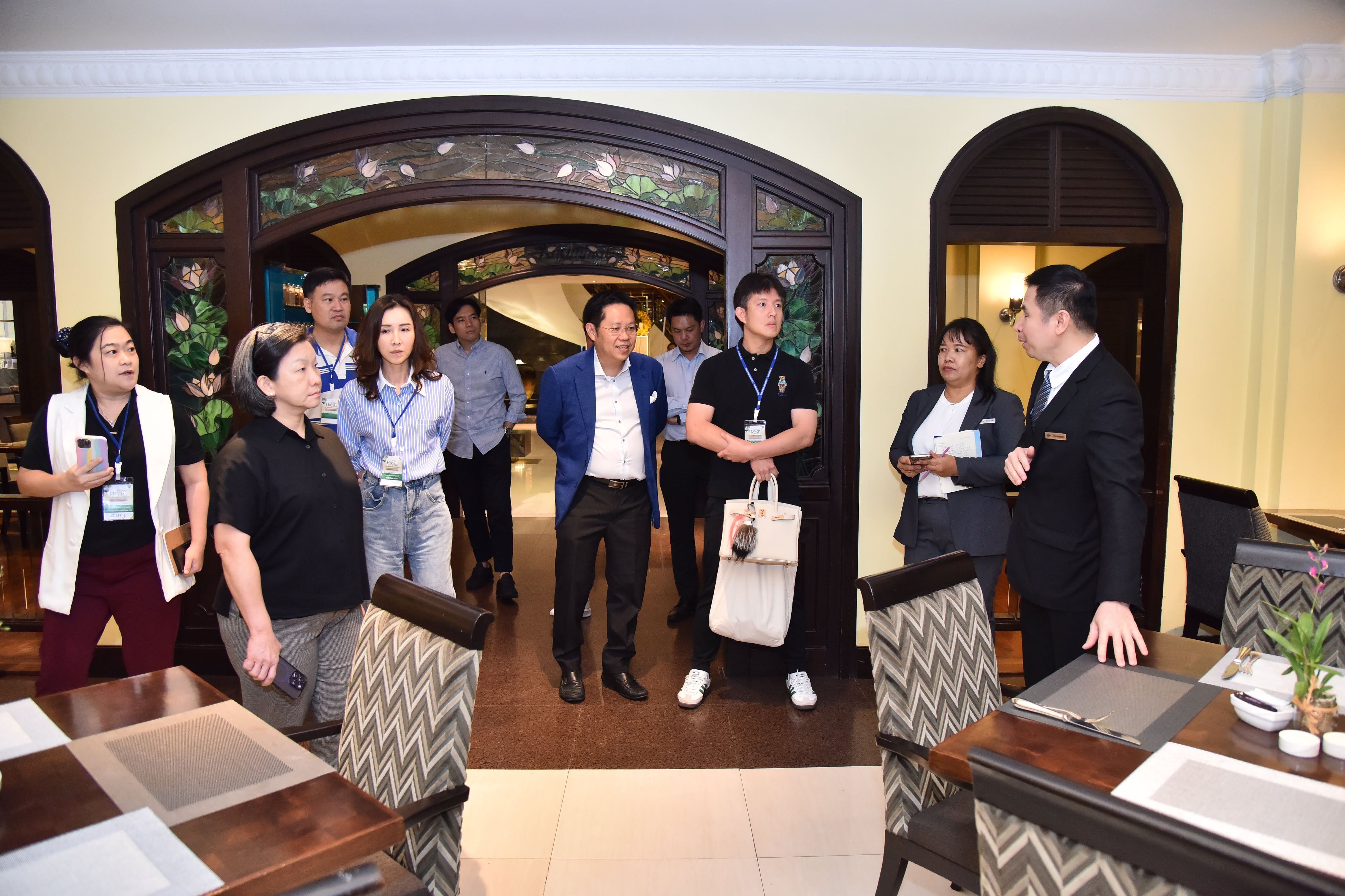 A group of professionals stands in a restaurant entrance, listening to a man in a dark suit.