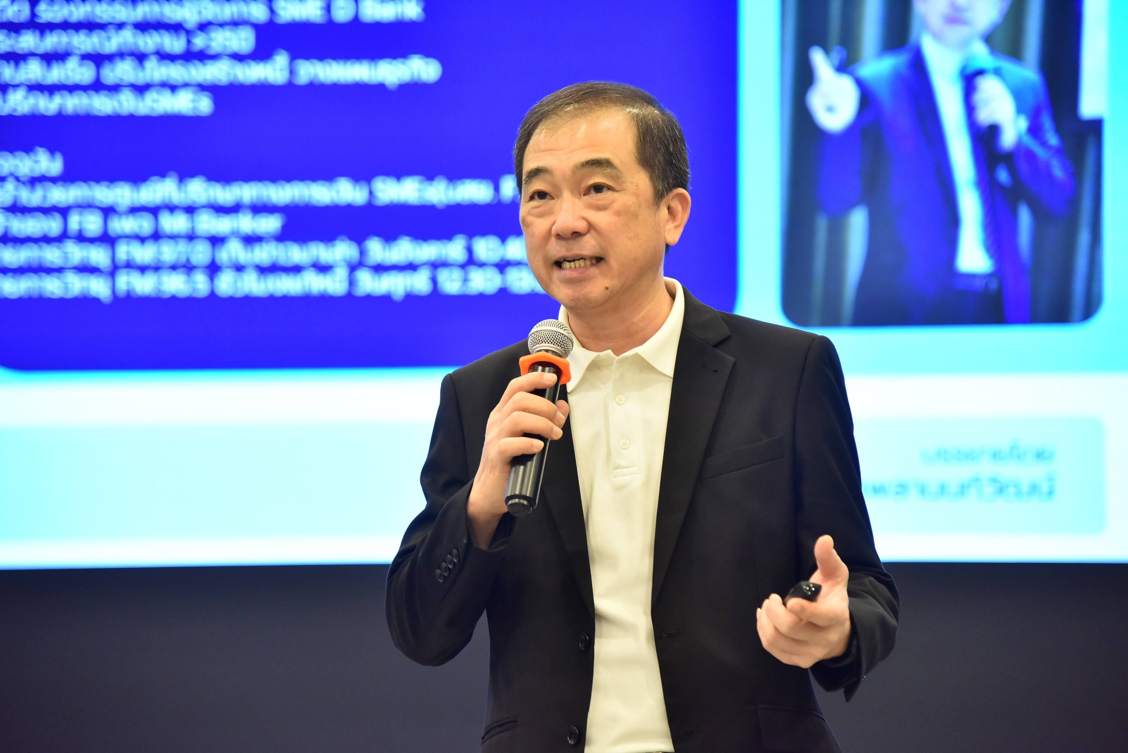 Man speaking into microphone during a presentation with a blue screen backdrop.