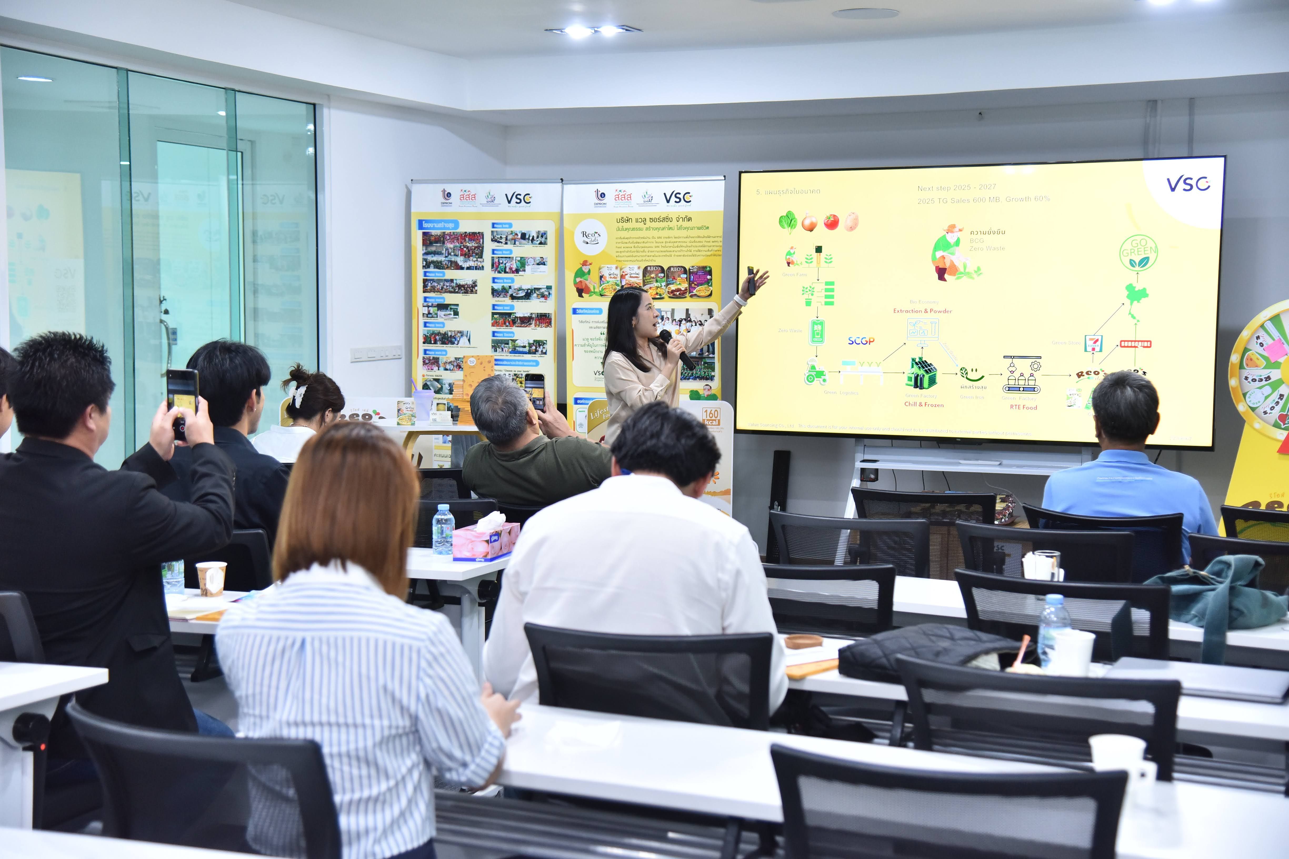 Woman presenting data on a large screen to an audience in a bright meeting room.