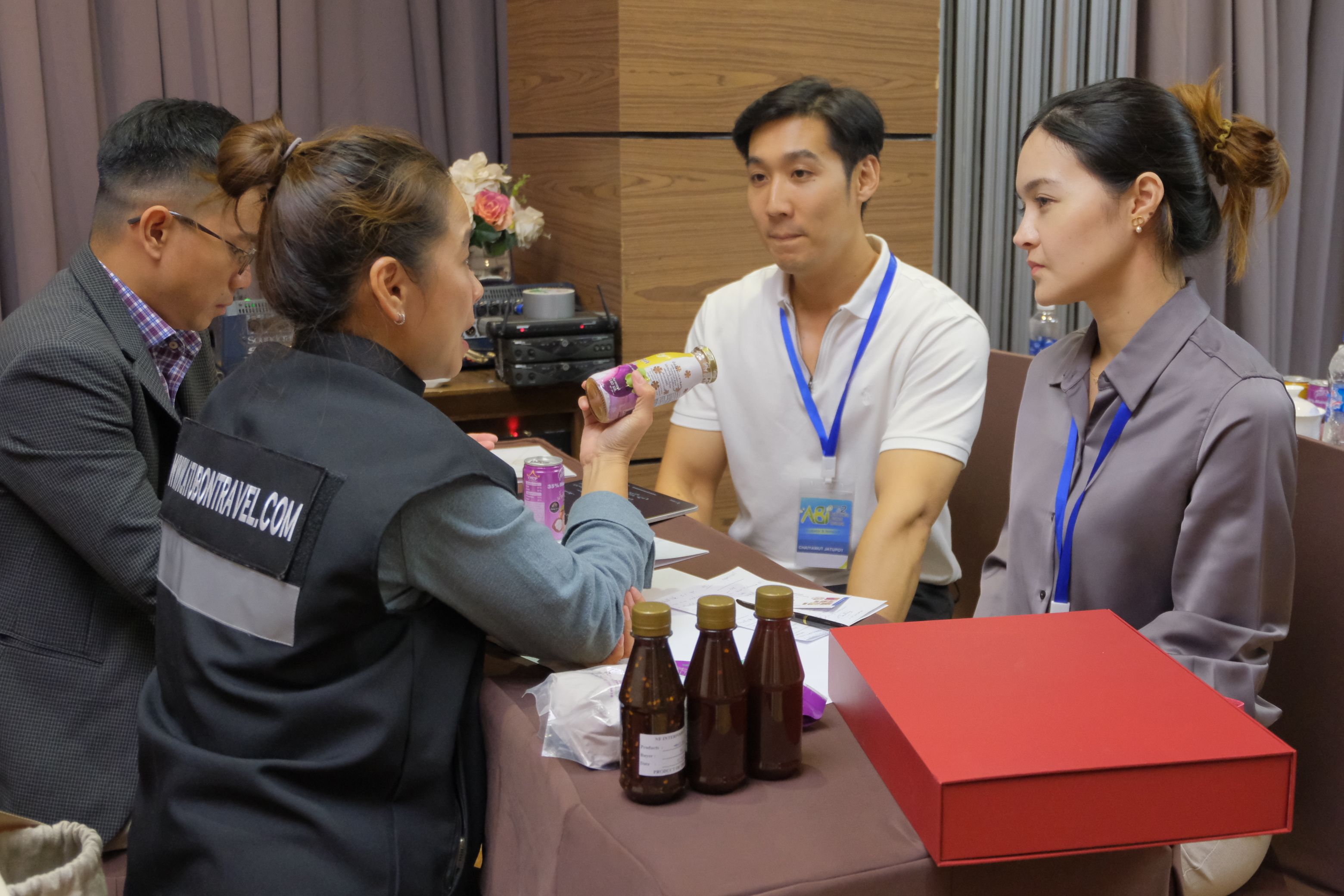 A woman in a black vest presents a bottled product to a man and woman at a table.