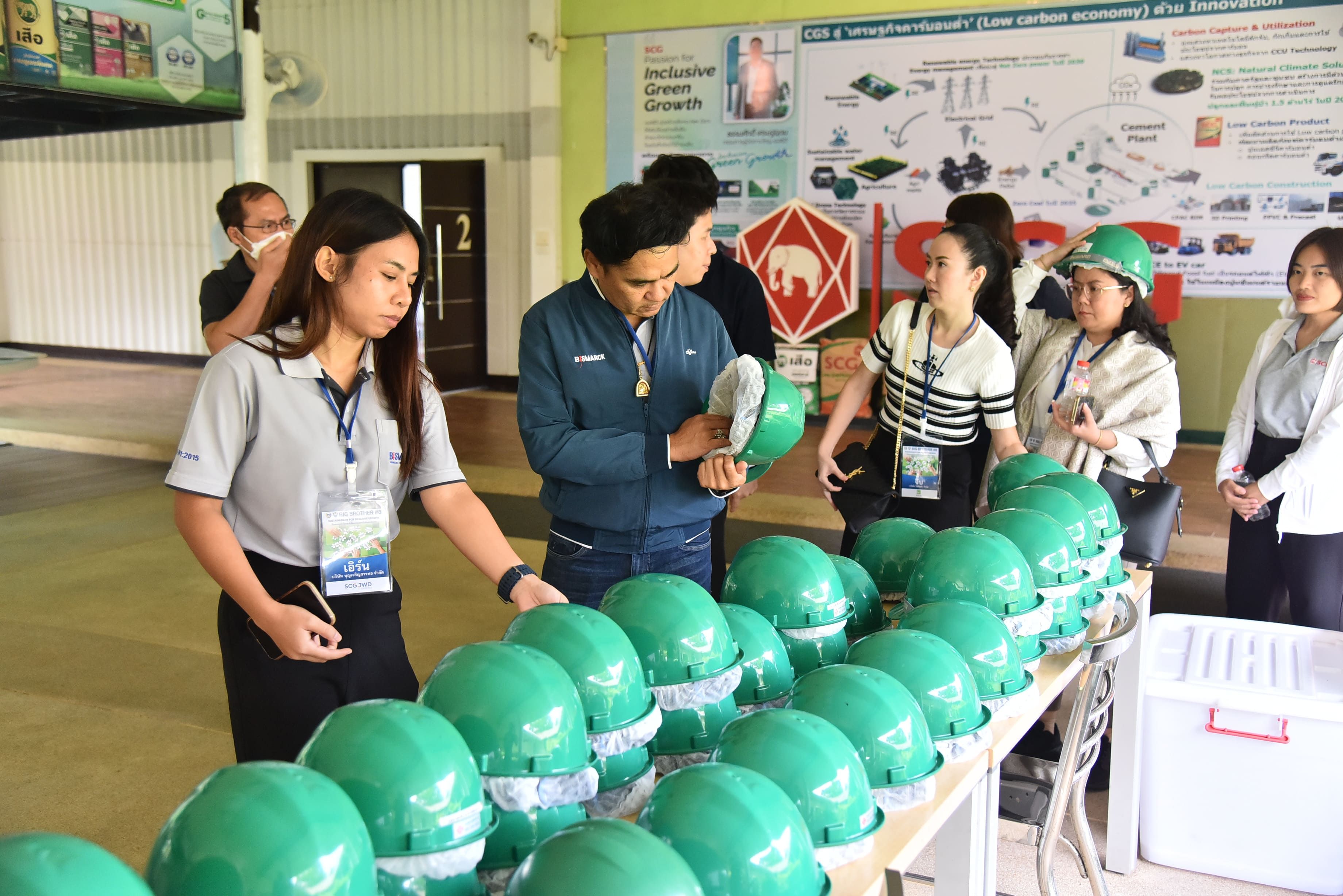A group of individuals selects green safety hard hats from a table for an industrial facility tour.