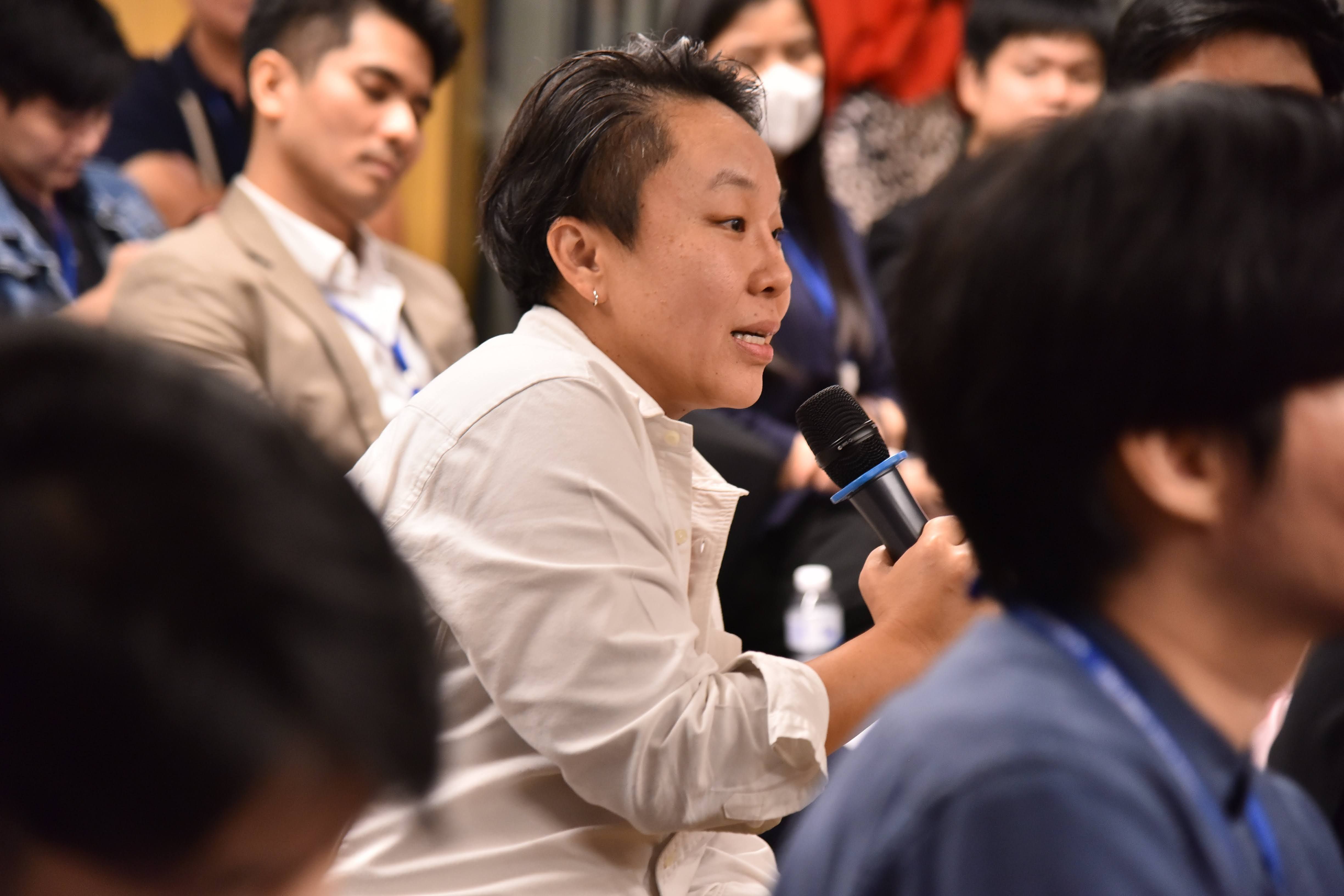 Person with short dark hair speaks into a microphone at a public event.