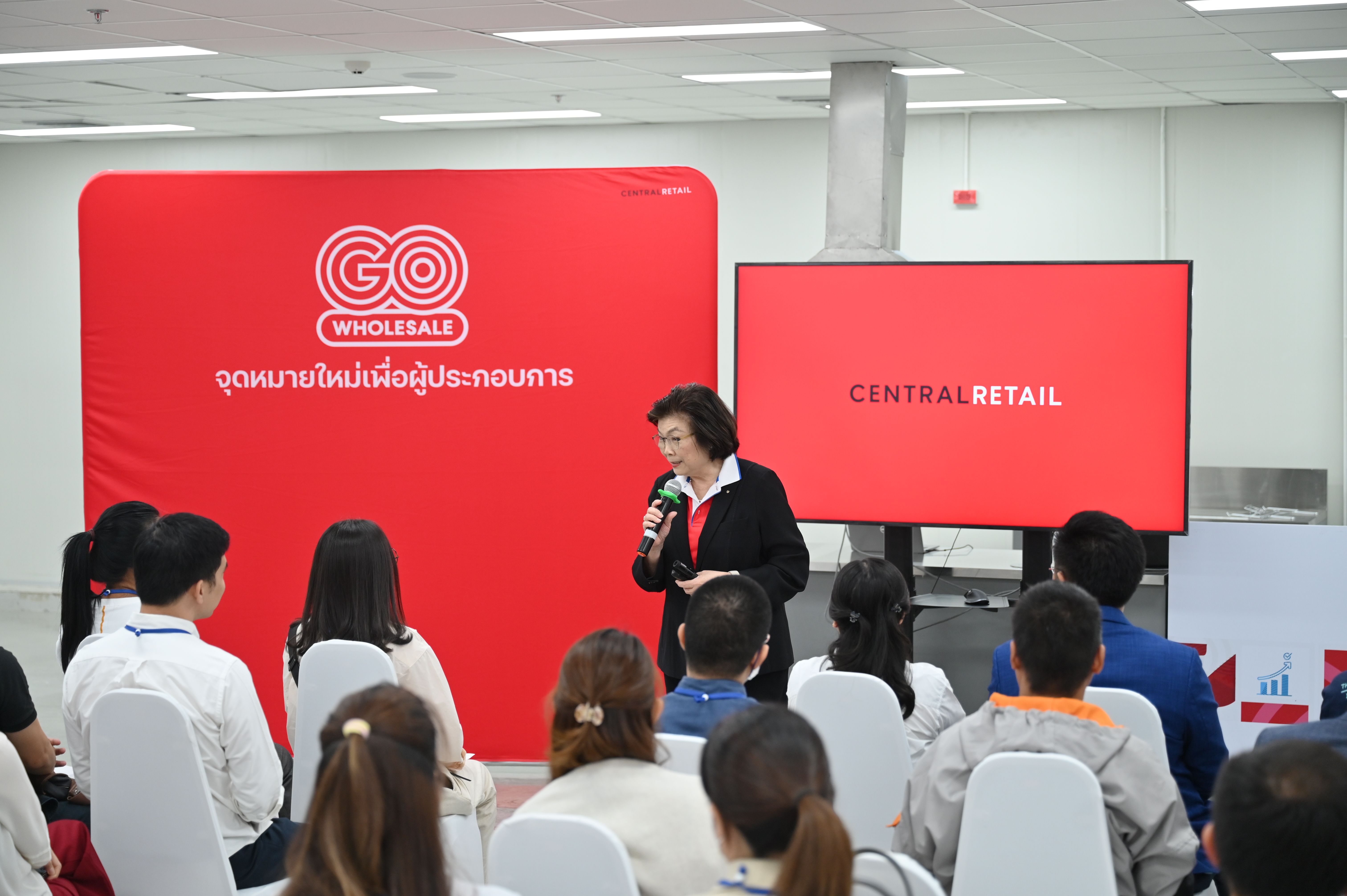 Woman speaks at a GO WHOLESALE event with 'Central Retail' displayed on a screen.