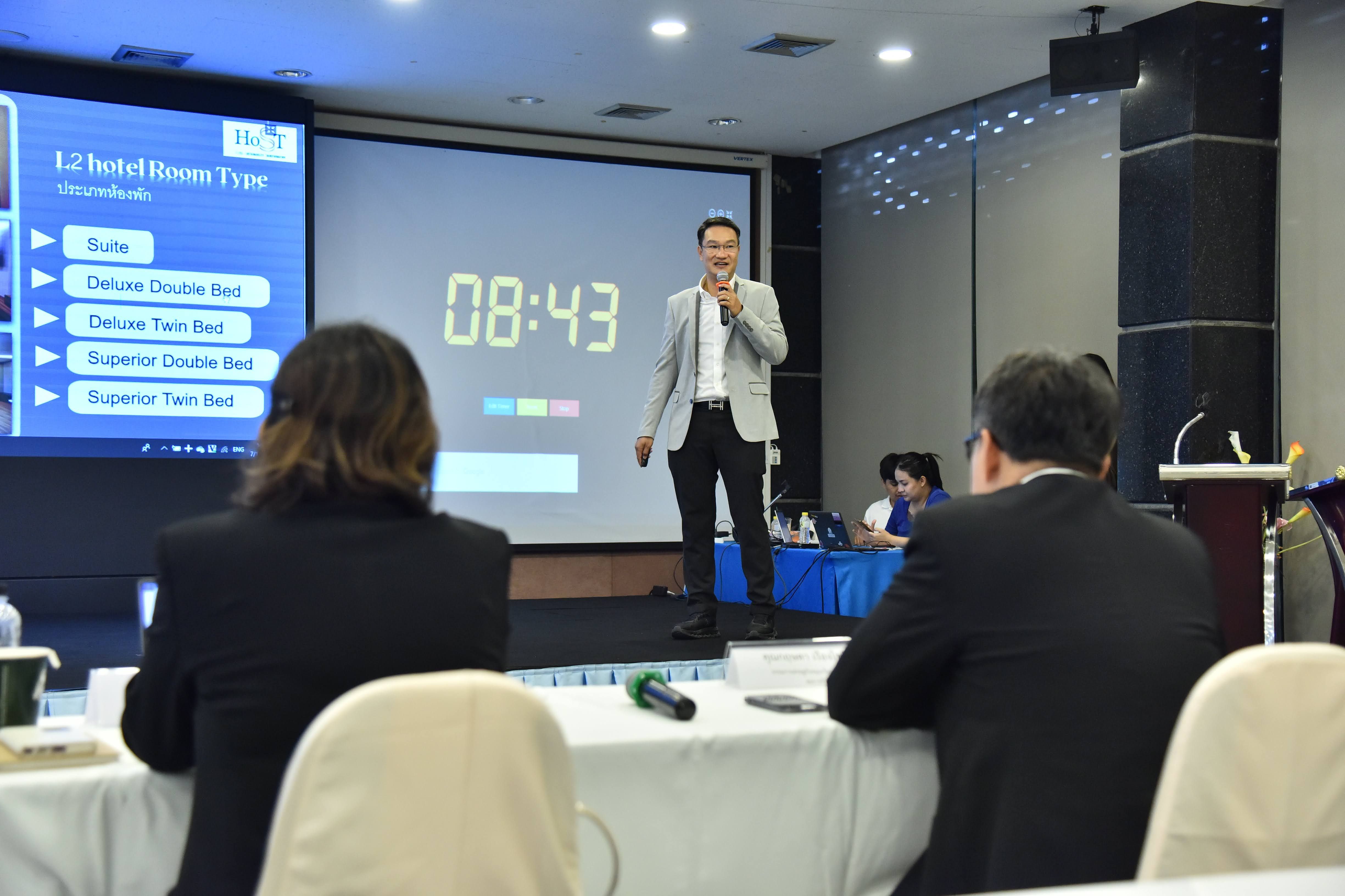 Speaker presents on stage with a large digital timer and presentation screens.