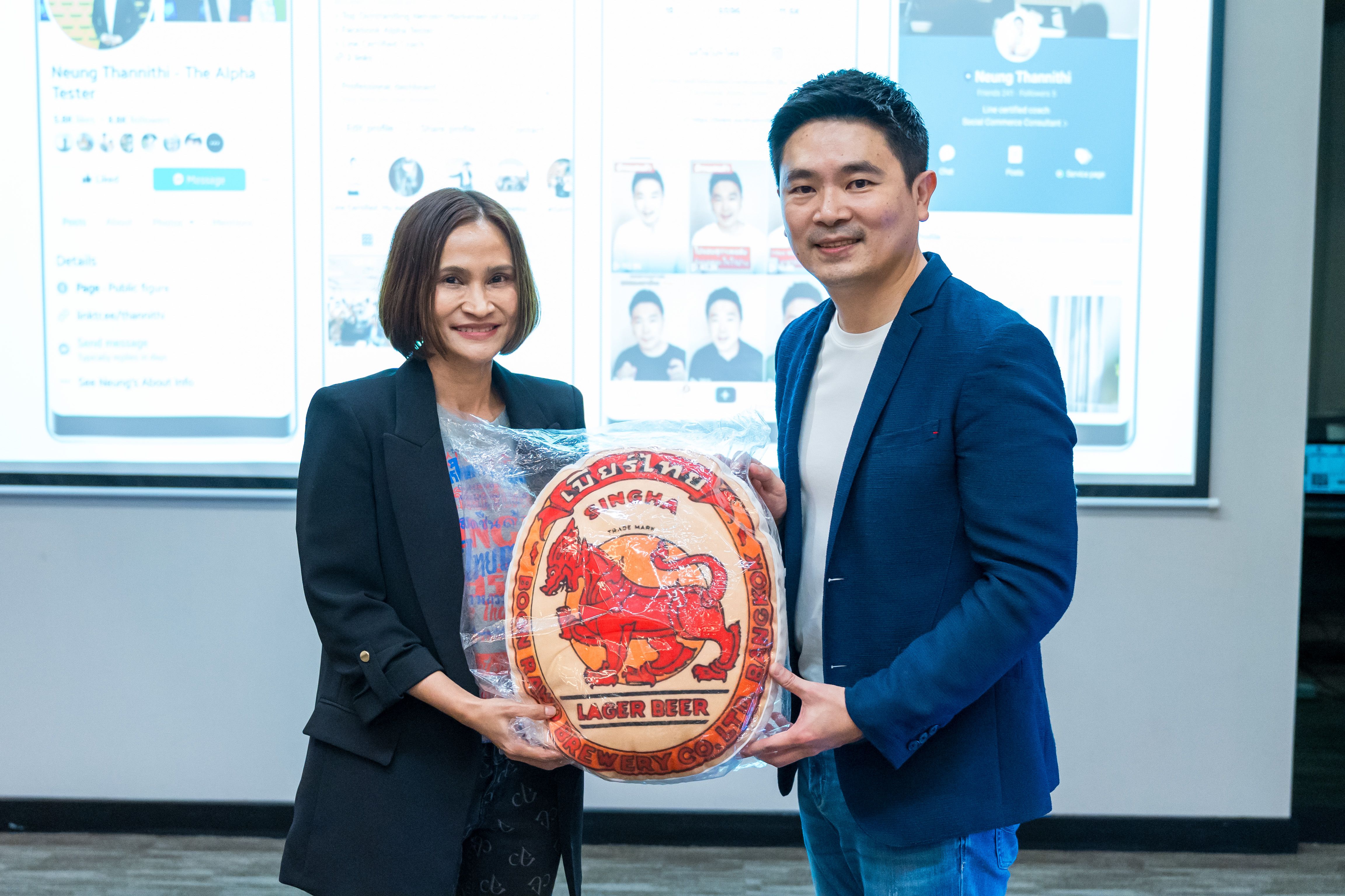 Two professionals holding a red San Miguel Beer award, smiling in an office setting.