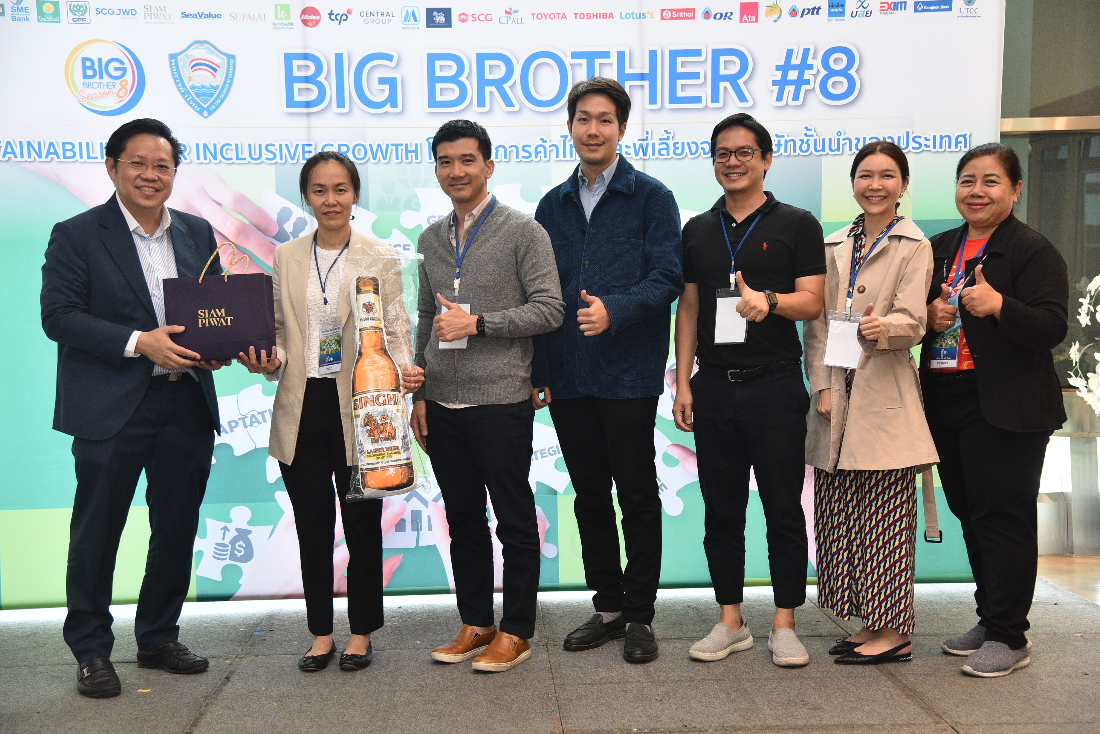 Eight people pose on stage at the 'BIG BROTHER #8' event, some holding awards.