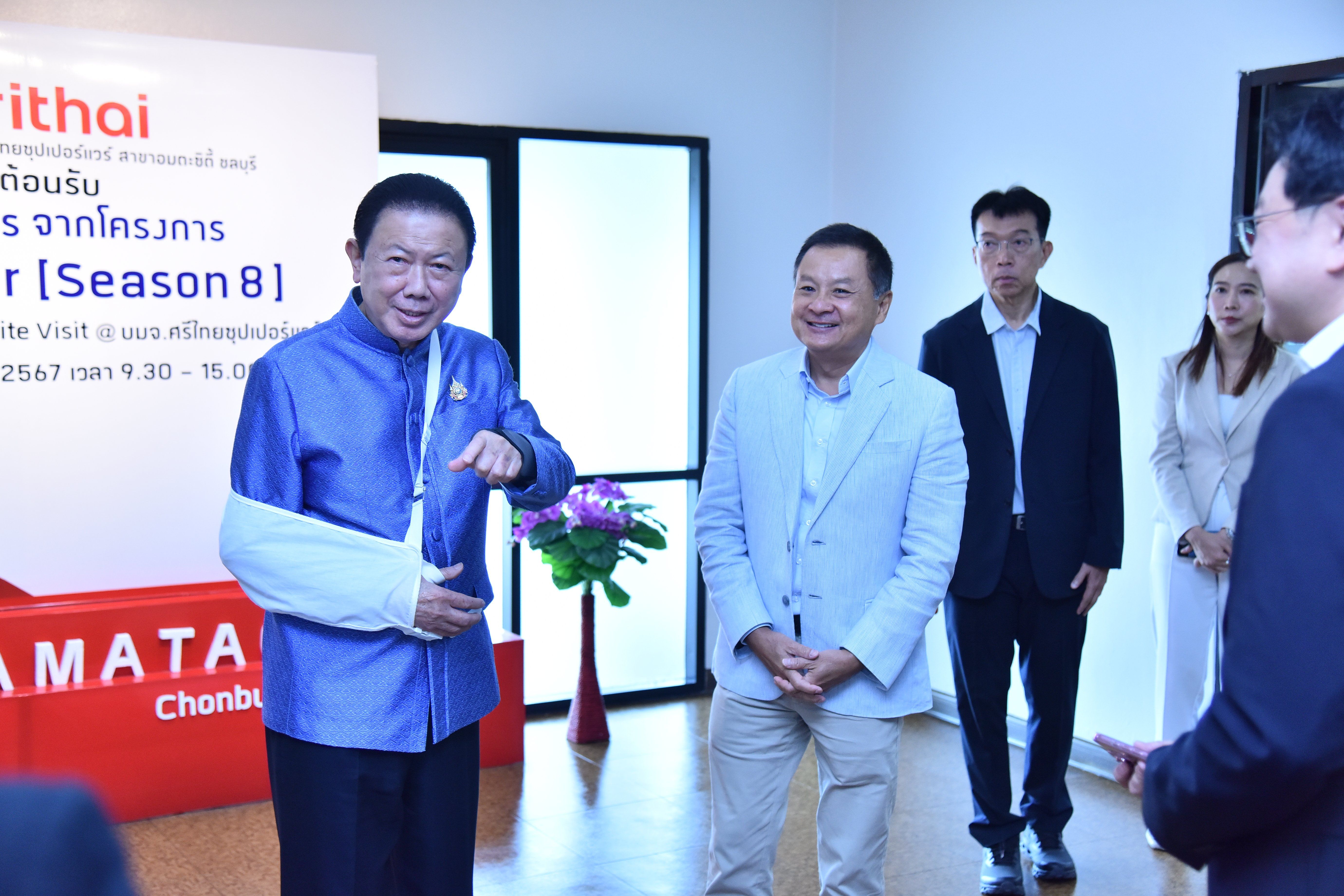 Man in blue shirt with arm cast smiles, gesturing beside another man.