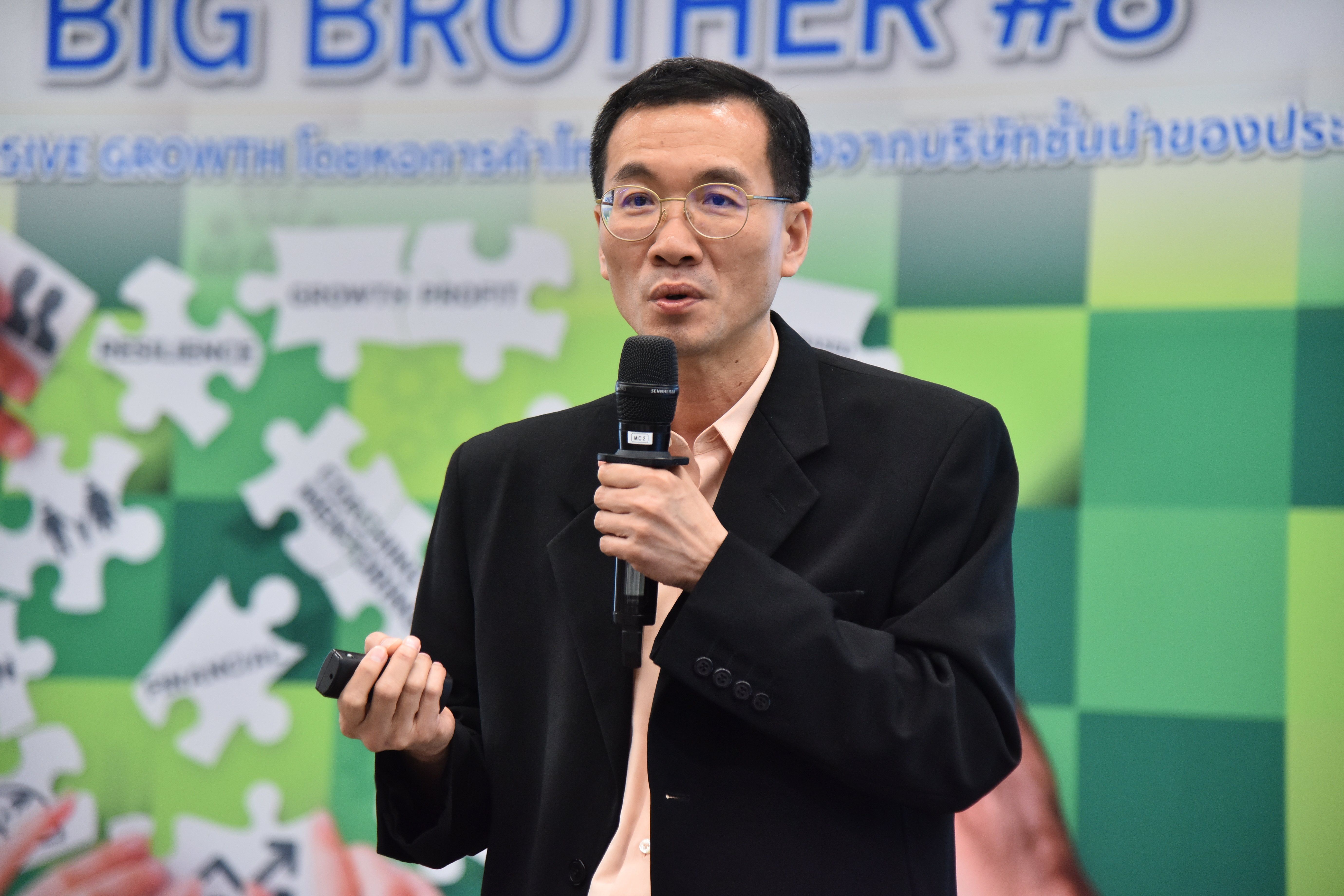 Professional man speaking into a microphone with a blurred presentation background.