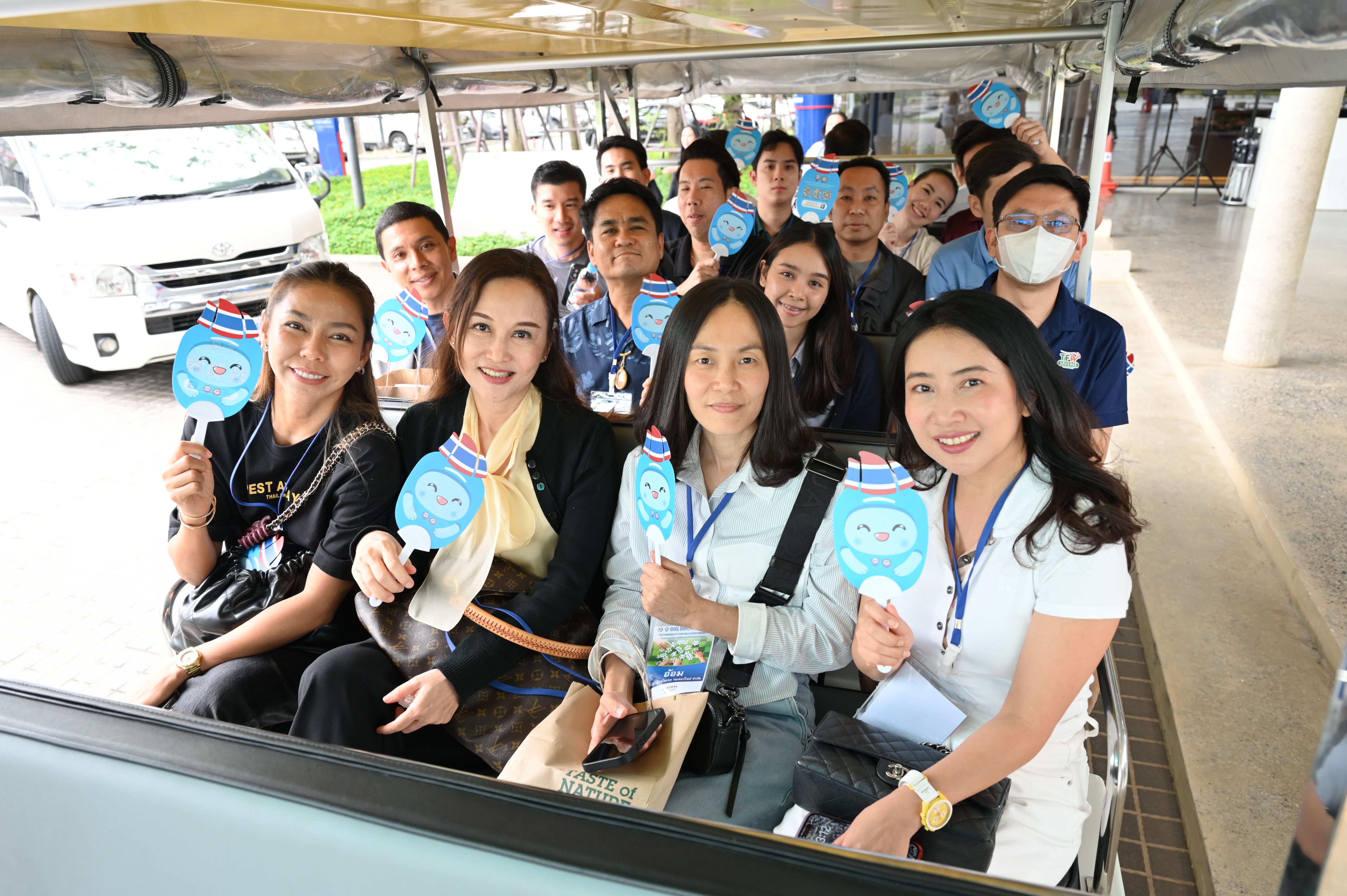 A group of smiling attendees rides an open-sided vehicle, holding blue cloud-shaped signs.