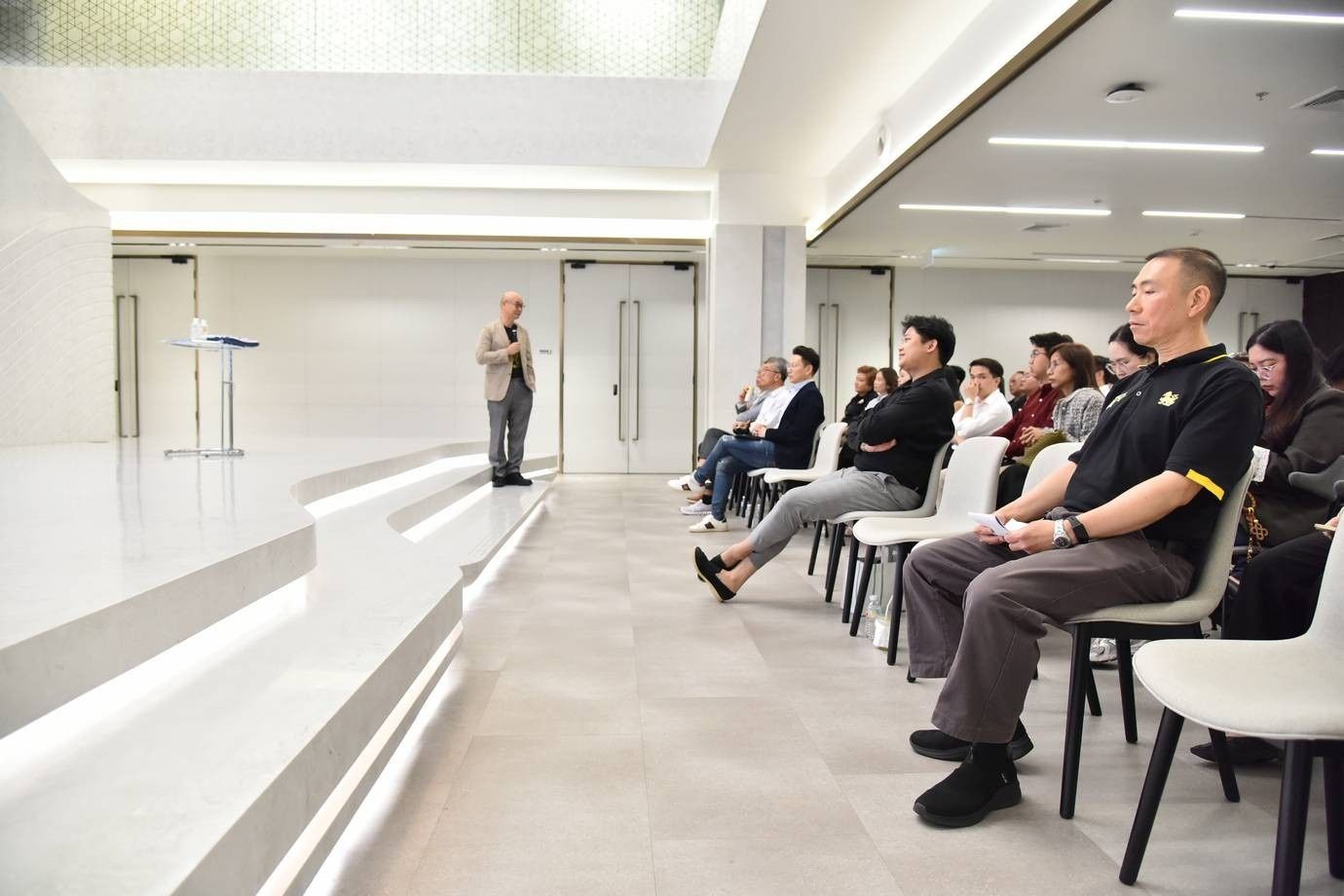 Speaker addresses an attentive audience in a modern, brightly lit conference room.