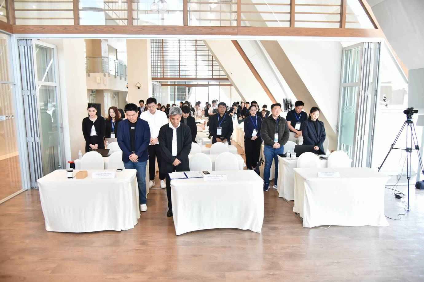 Professionals stand attentively behind white-draped tables in a bright conference room.