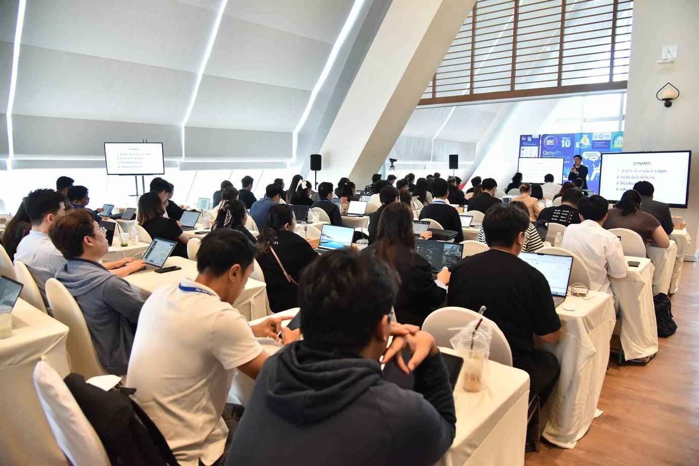 Attendees watch a presentation in a modern conference room with laptops.