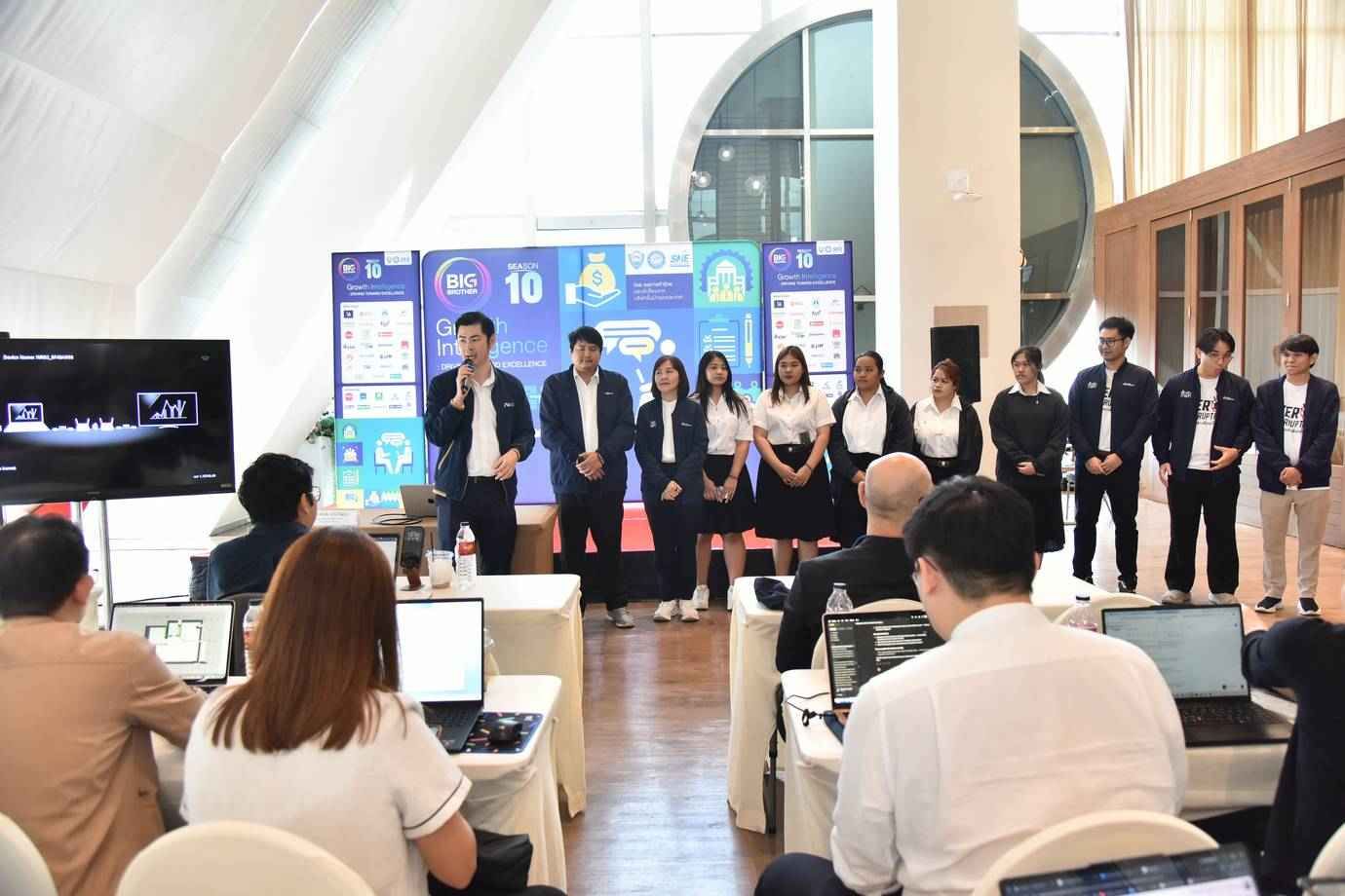 Students presenting on stage at an academic event with a screen and audience members.
