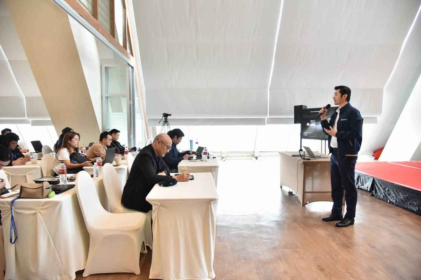 Man presenting with a microphone to an audience seated at tables during a conference.