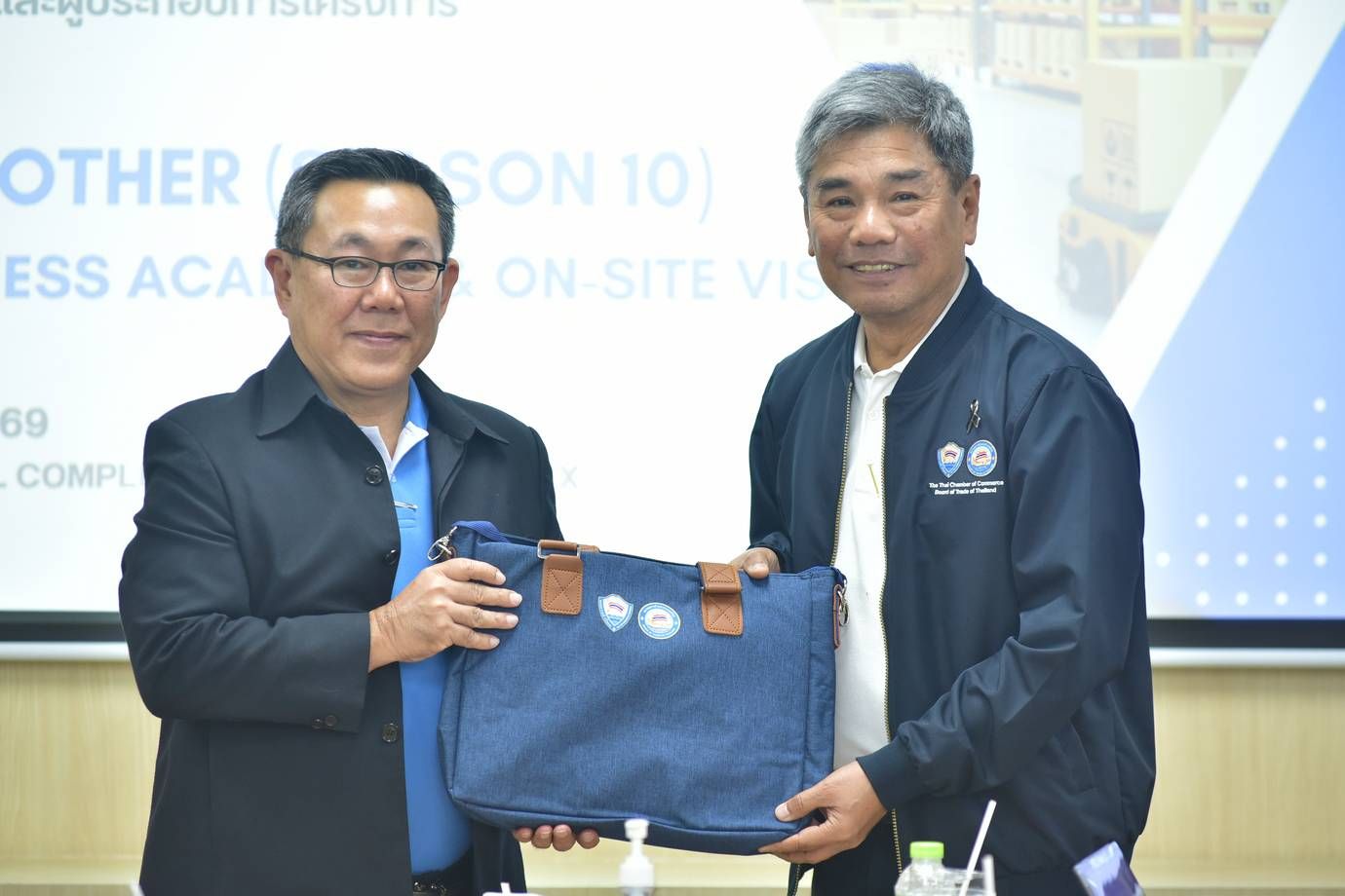Two professional men, one handing a blue bag to the other in an office setting.