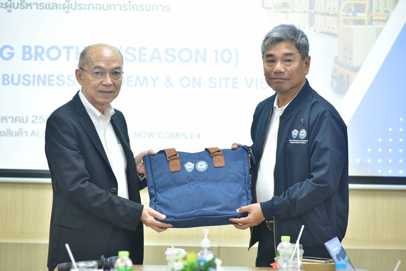 Two men exchange a blue bag, symbolizing partnership at a business event.