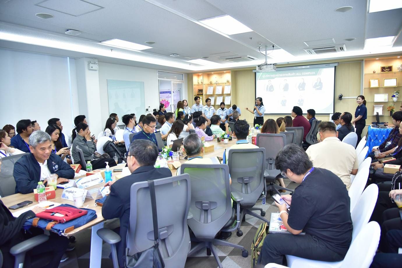 Professionals attend a presentation in a modern conference room with a speaker and projector screen.