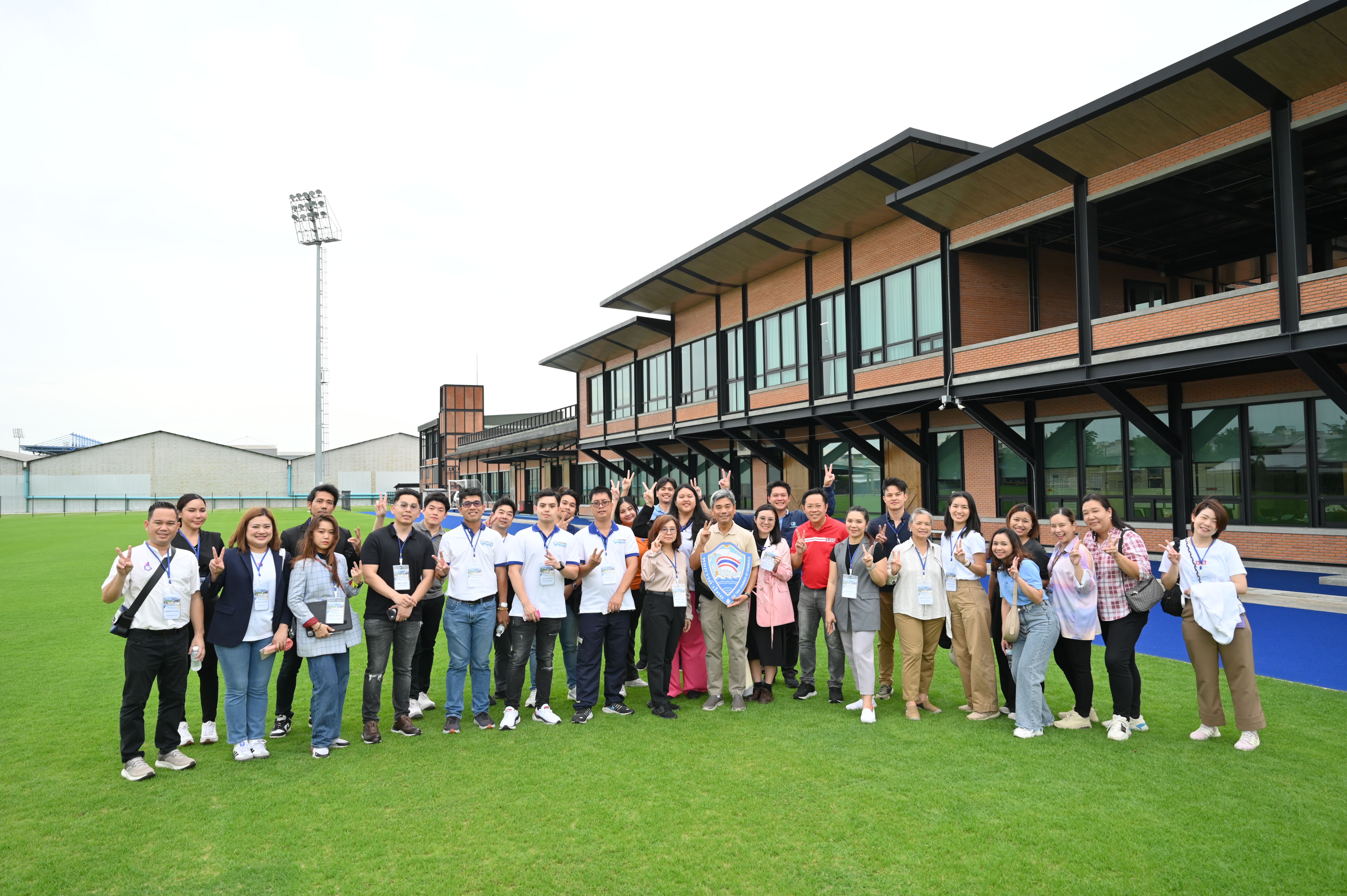 Large group of professionals standing on a green field in front of a modern building.