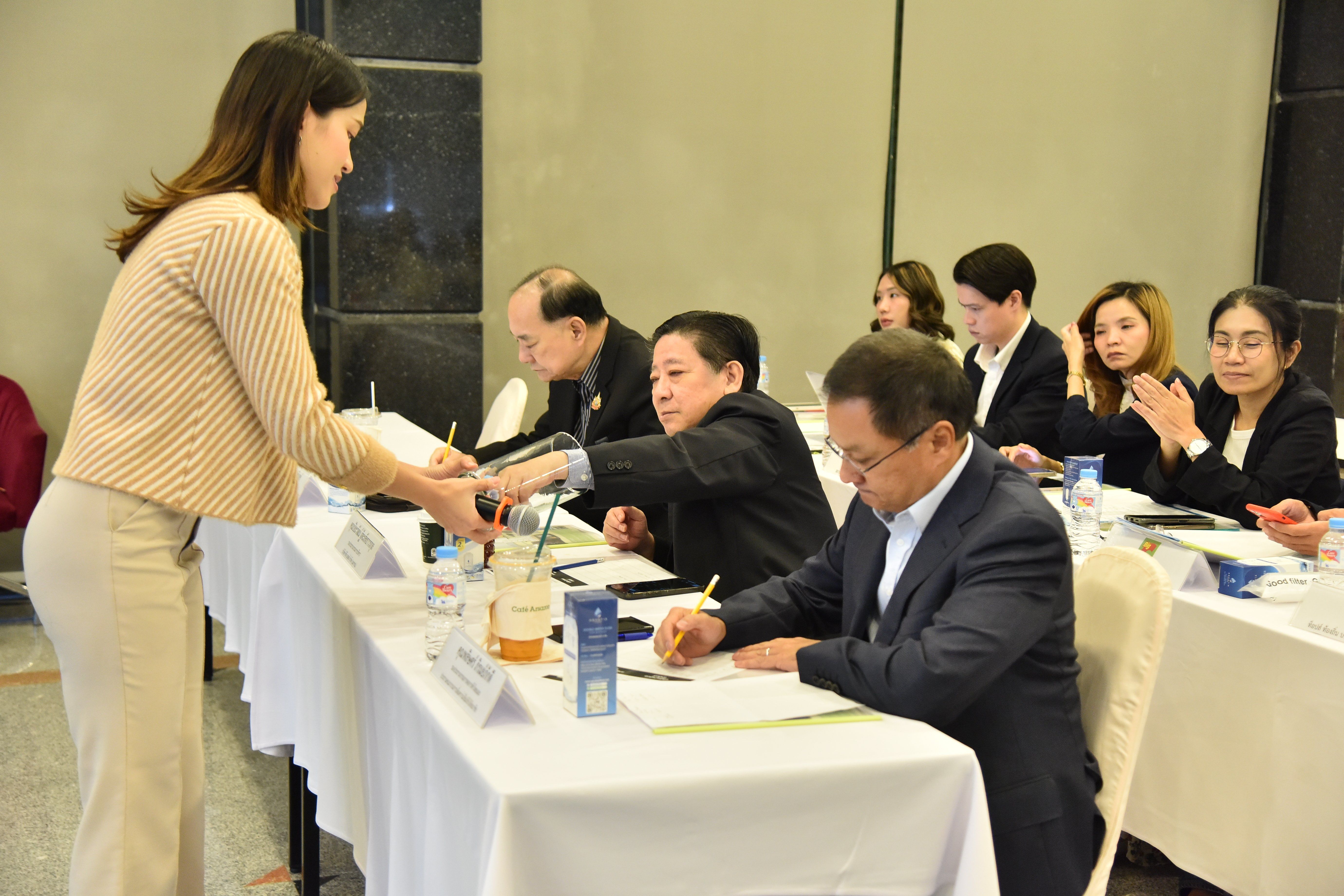Woman serves beverages to professionals seated at a long table during a meeting.