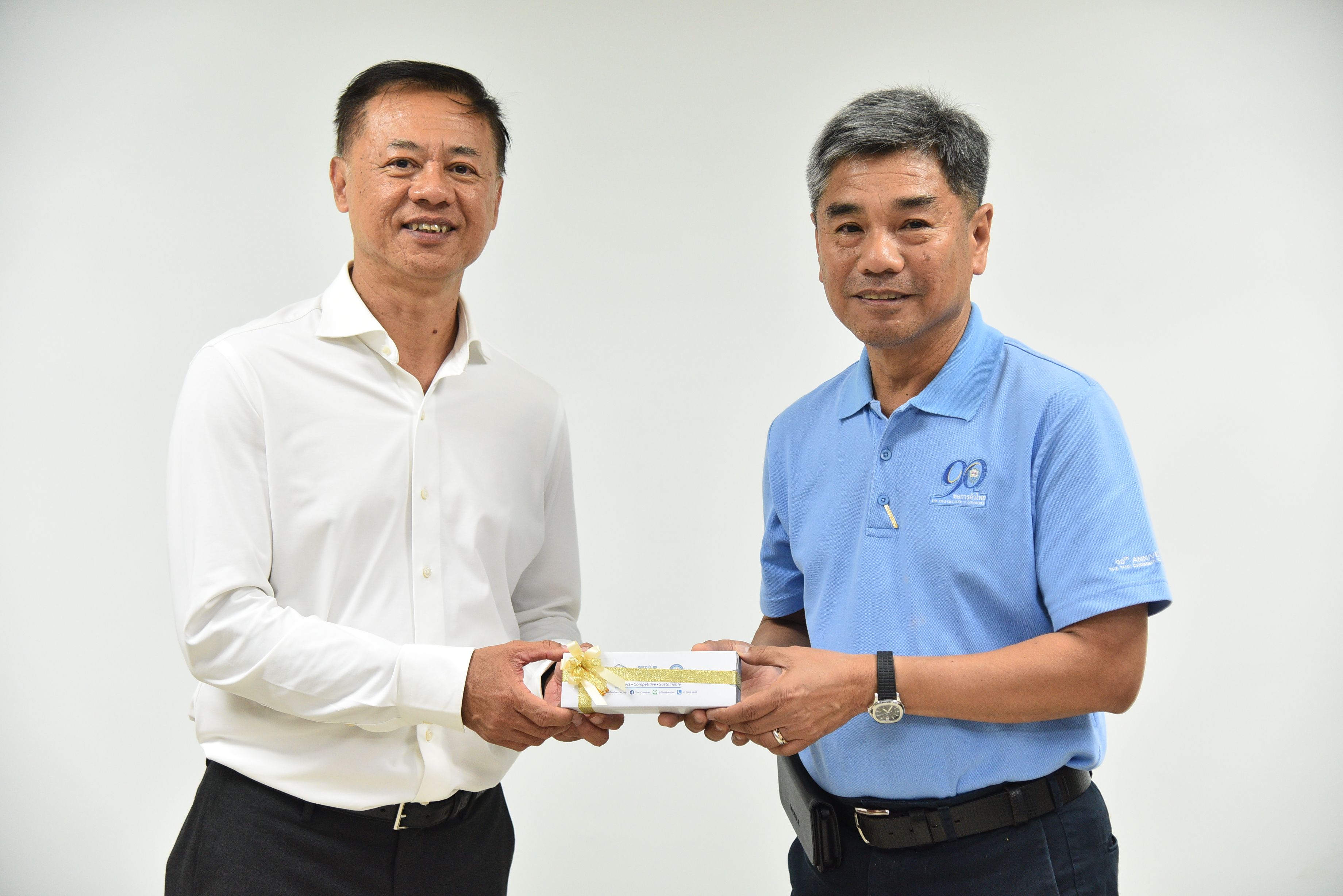 Two professional men smiling while exchanging a small, elegantly wrapped gift box.