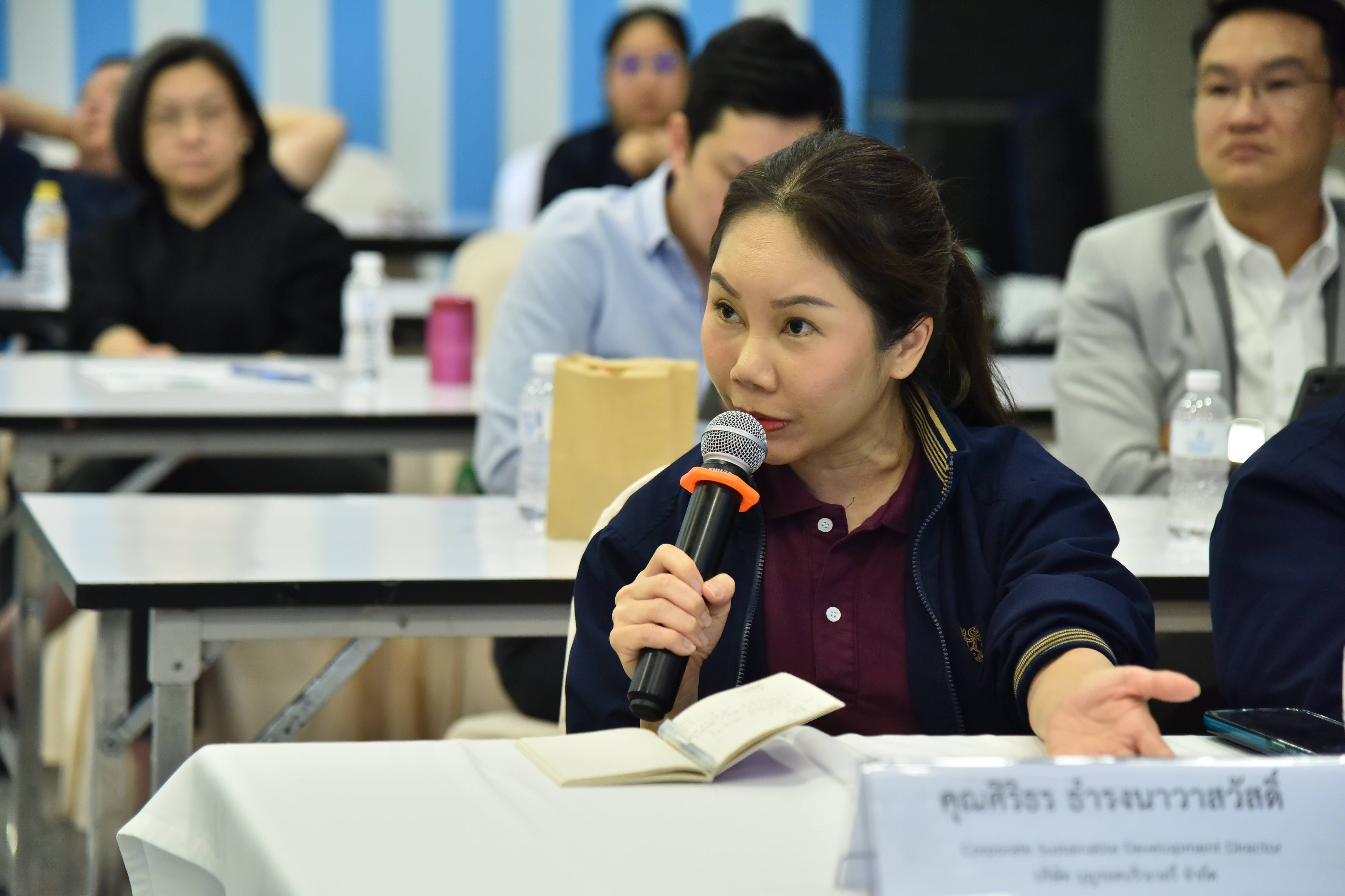 Woman speaks into a microphone at a table during a conference.
