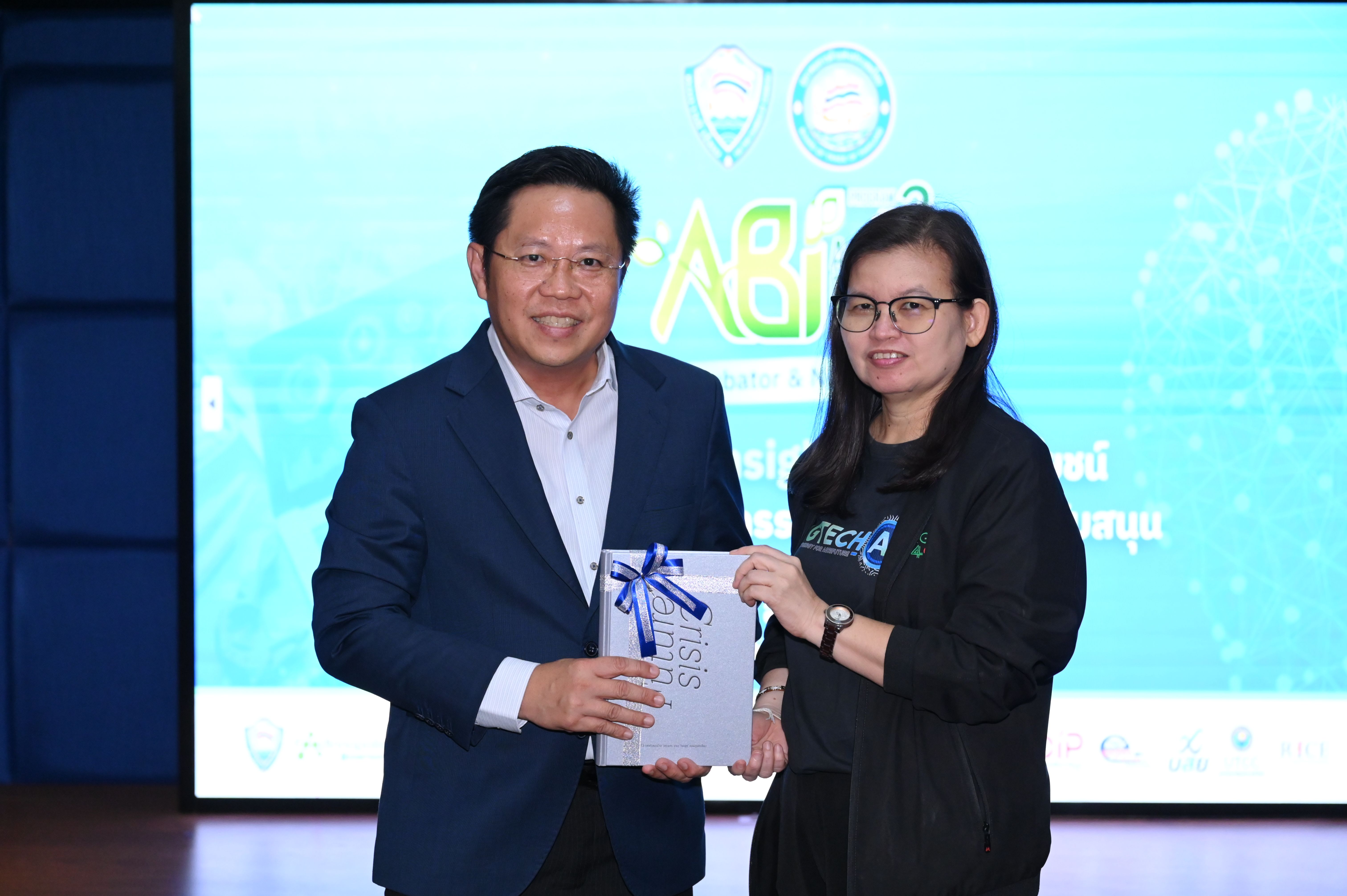 Man in blue suit presenting a gift box to a woman in glasses, both smiling.