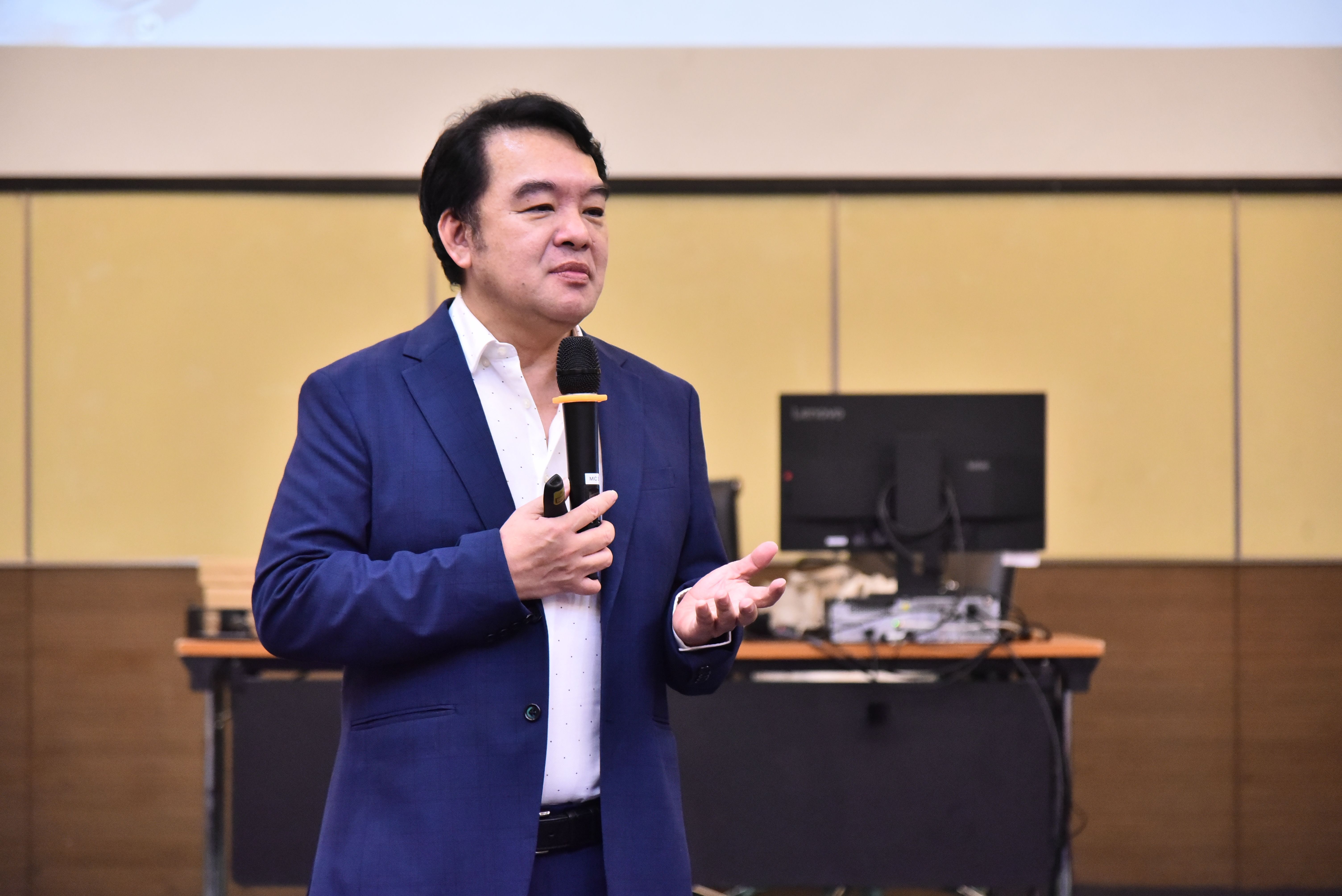 Man in blue suit speaking passionately into a microphone during a presentation.
