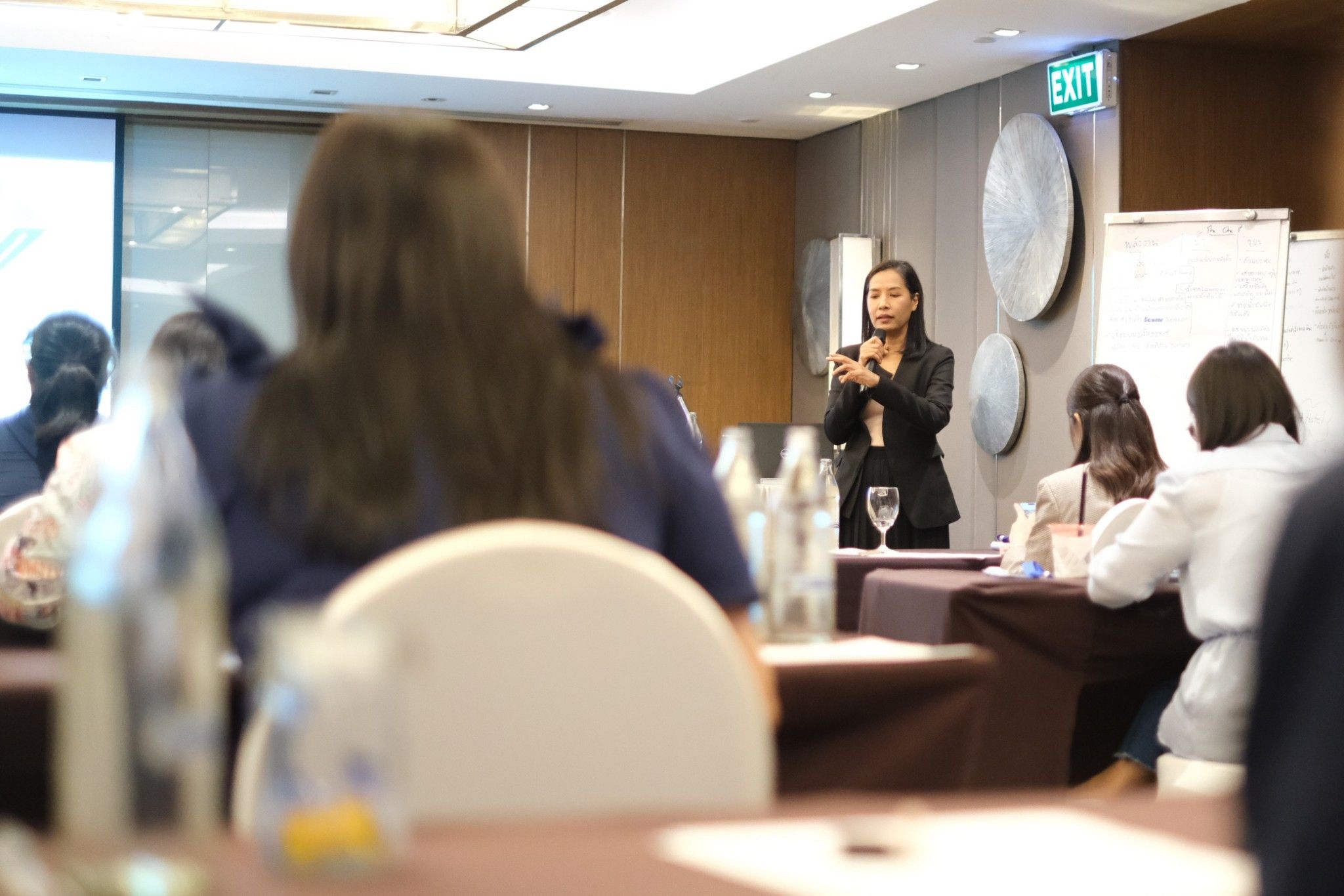 Woman in a suit speaks at a podium to an audience in a conference room.