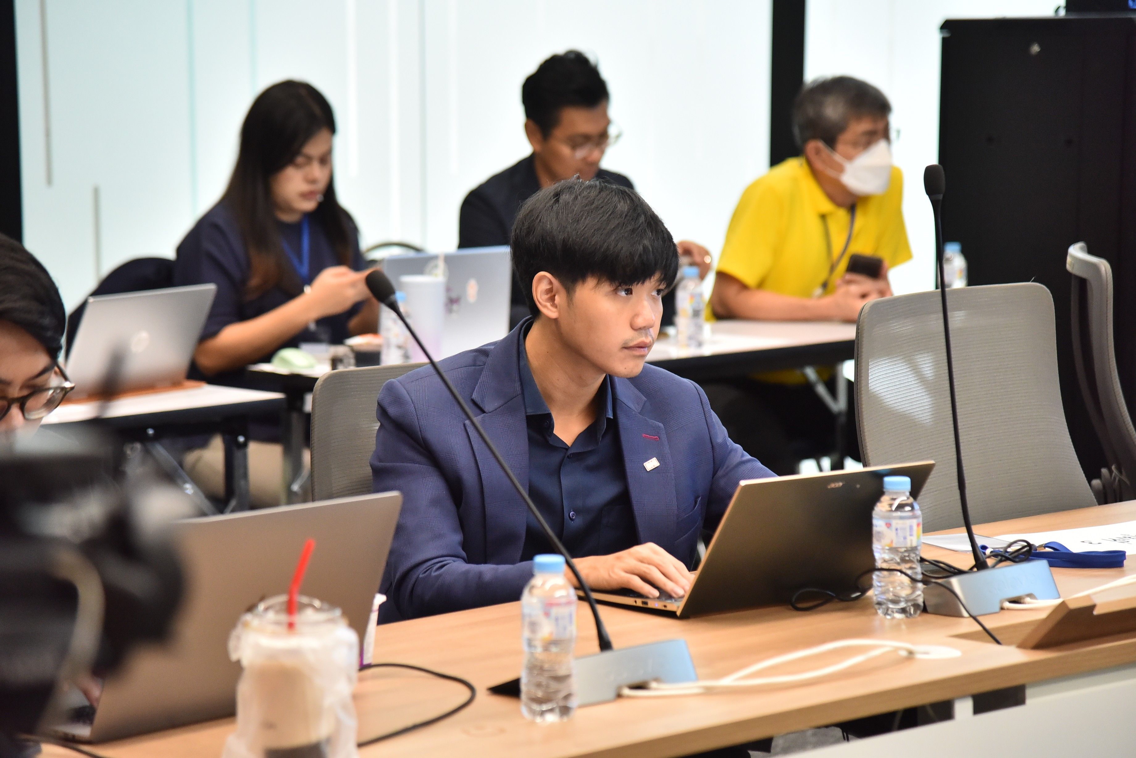 Man in blue jacket attending a professional meeting, focused on his laptop.