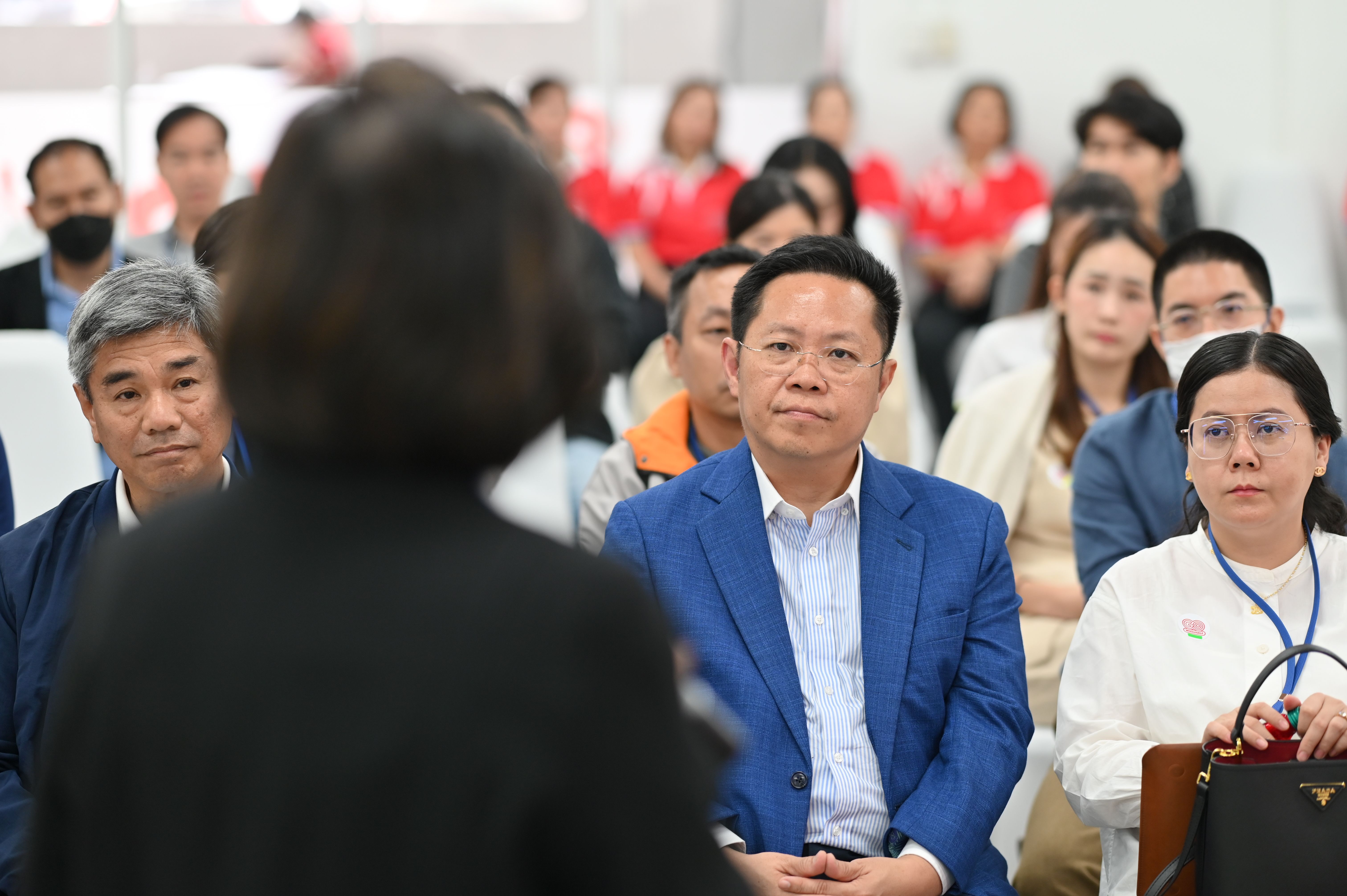Attendees at a conference attentively listening to a speaker in an indoor setting.