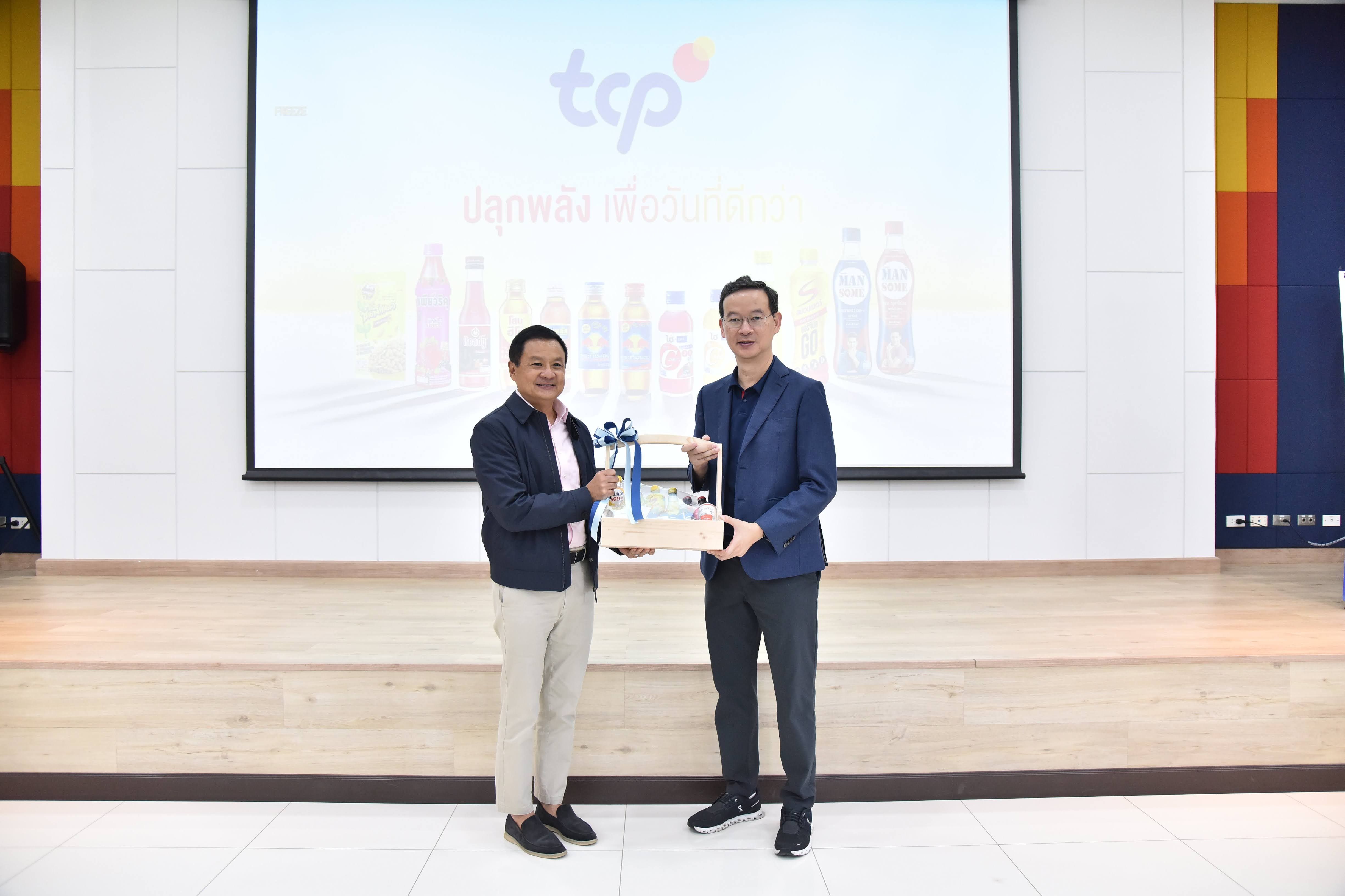 Two men exchange an award on a stage, a "tcp" logo projected behind them.