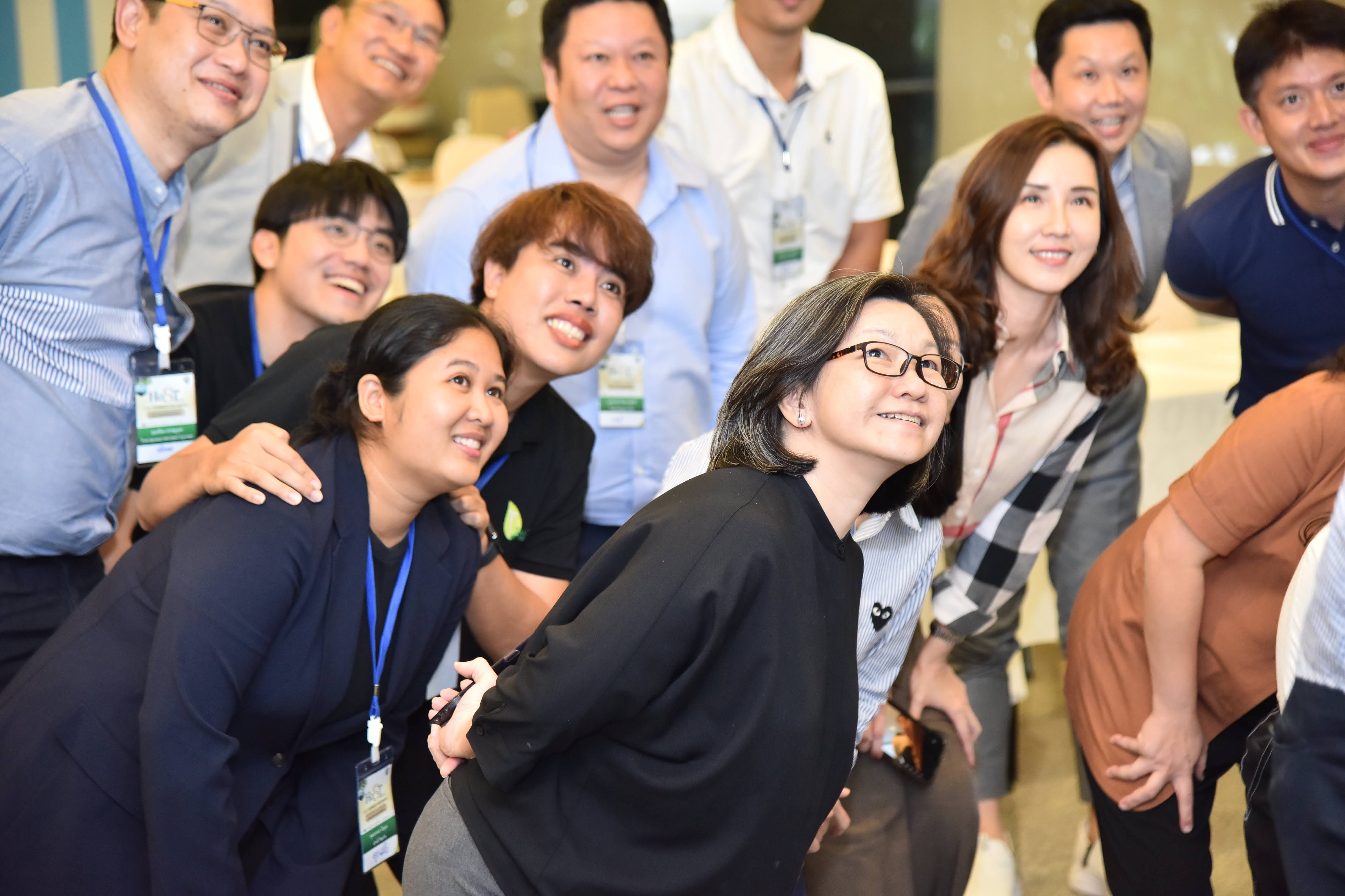 A diverse group of Asian people smiling and looking up, posing for a photo at an event.
