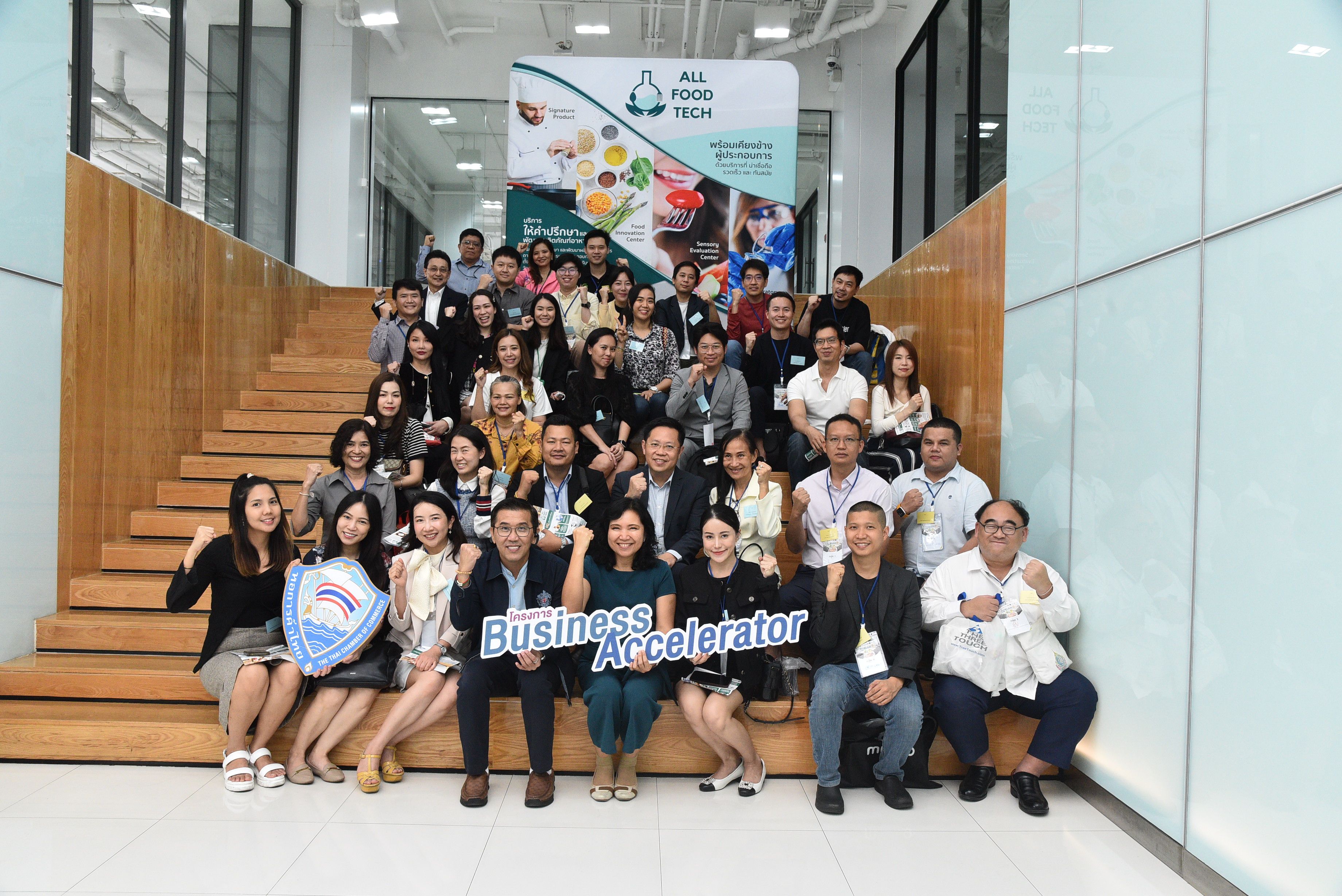 Smiling diverse group poses on stairs, holding a "Business Accelerator" sign.