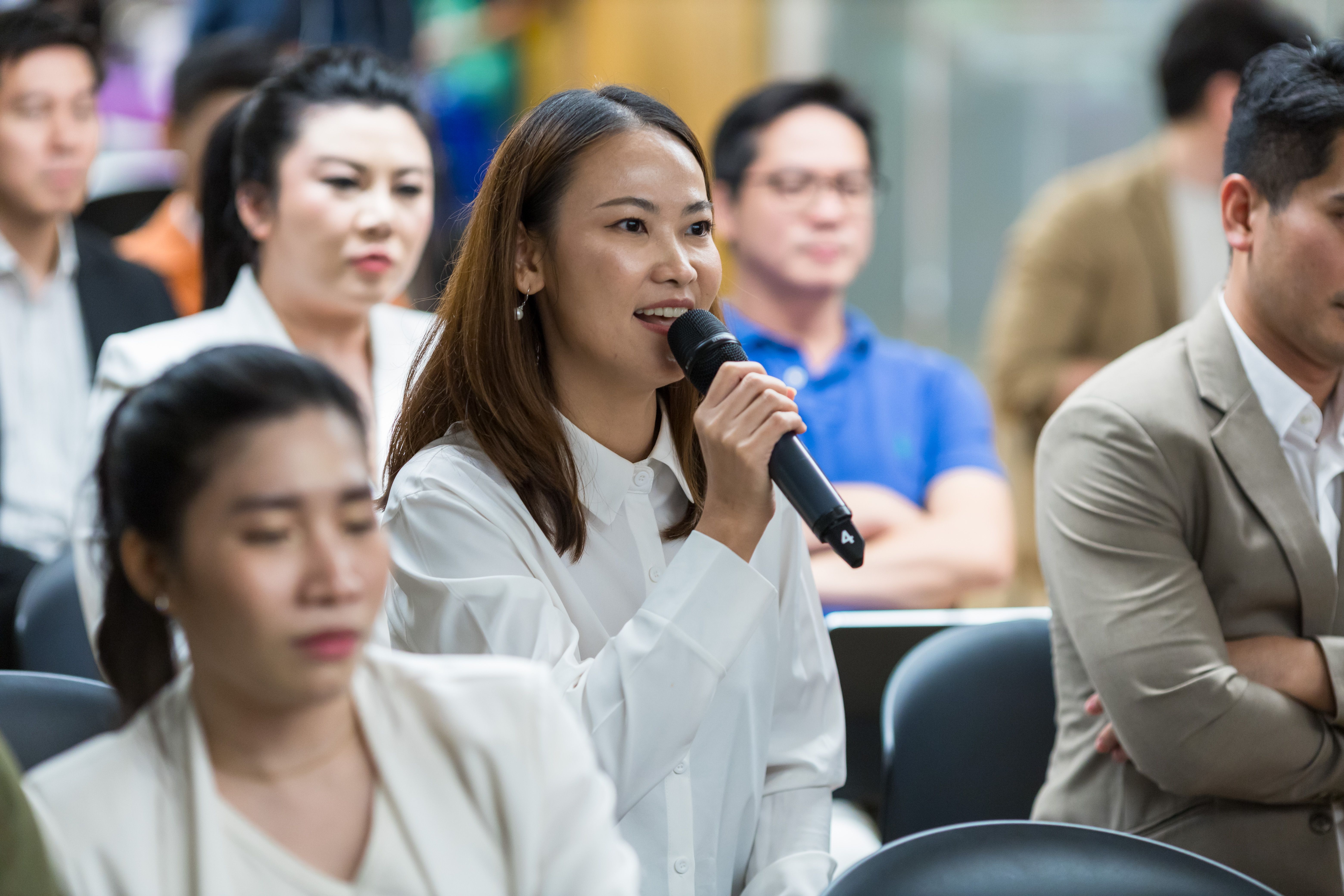 Young woman in a white shirt speaking into a microphone at a professional event.
