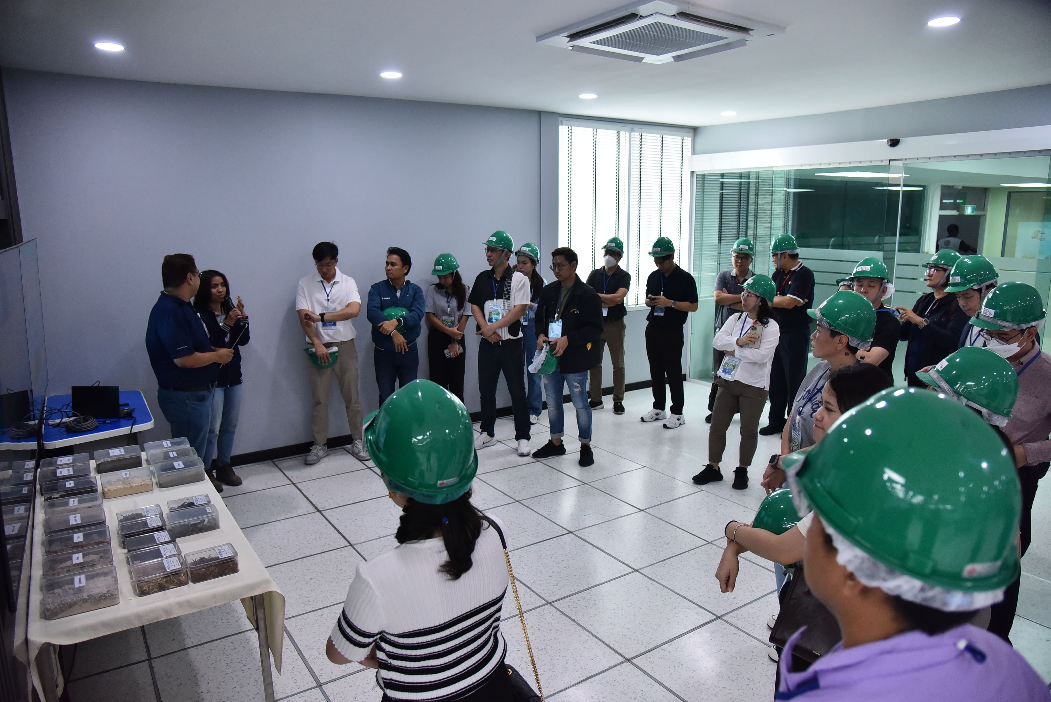 A group of people wearing green hard hats attend a presentation in a modern room.