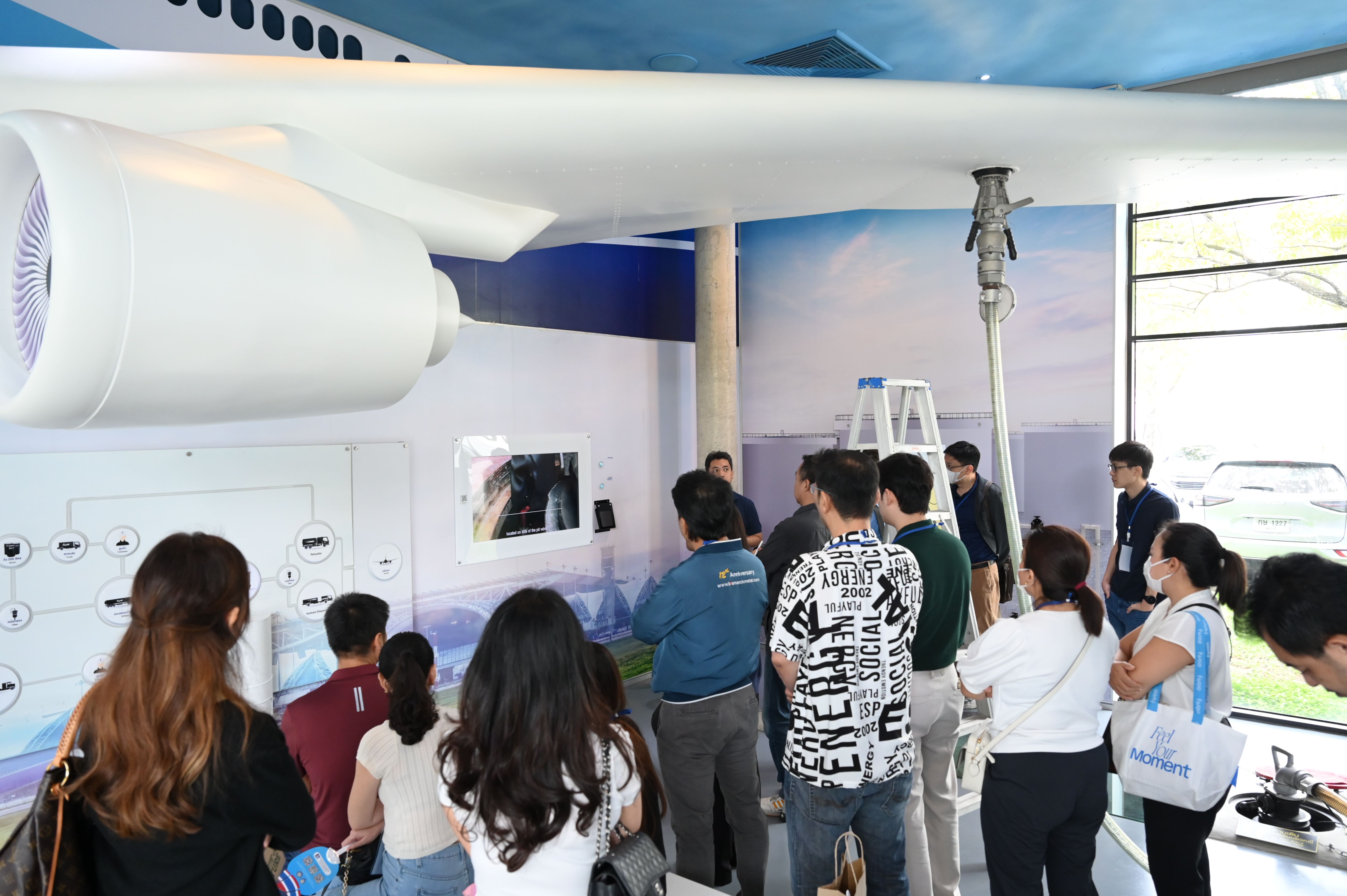 Group of people observing a large white airplane model with engine and interactive displays.