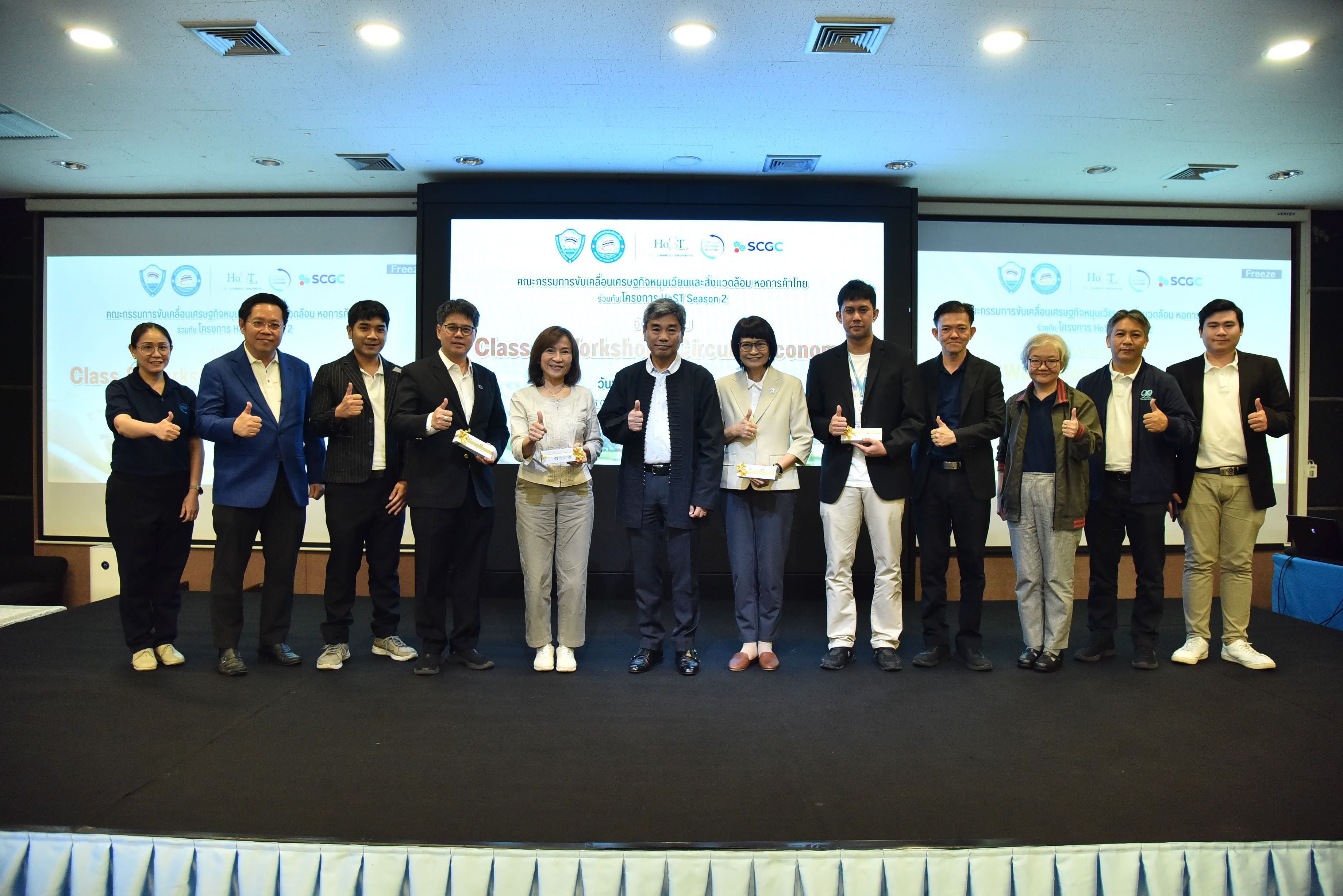 Thirteen professionals stand on a stage, some holding awards, at a formal indoor event.