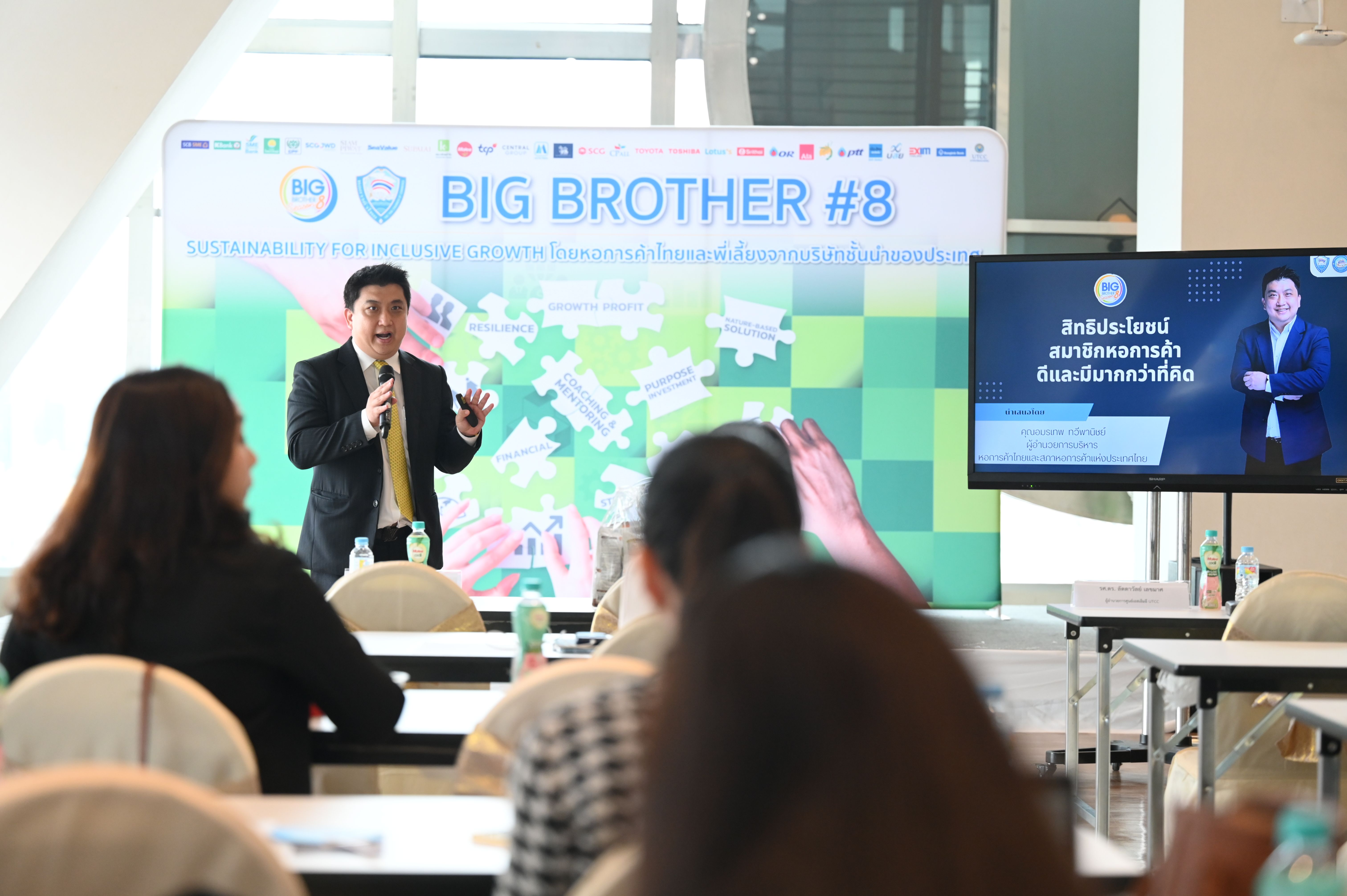 A man in a suit speaks at a podium during a "BIG BROTHER #8" event.