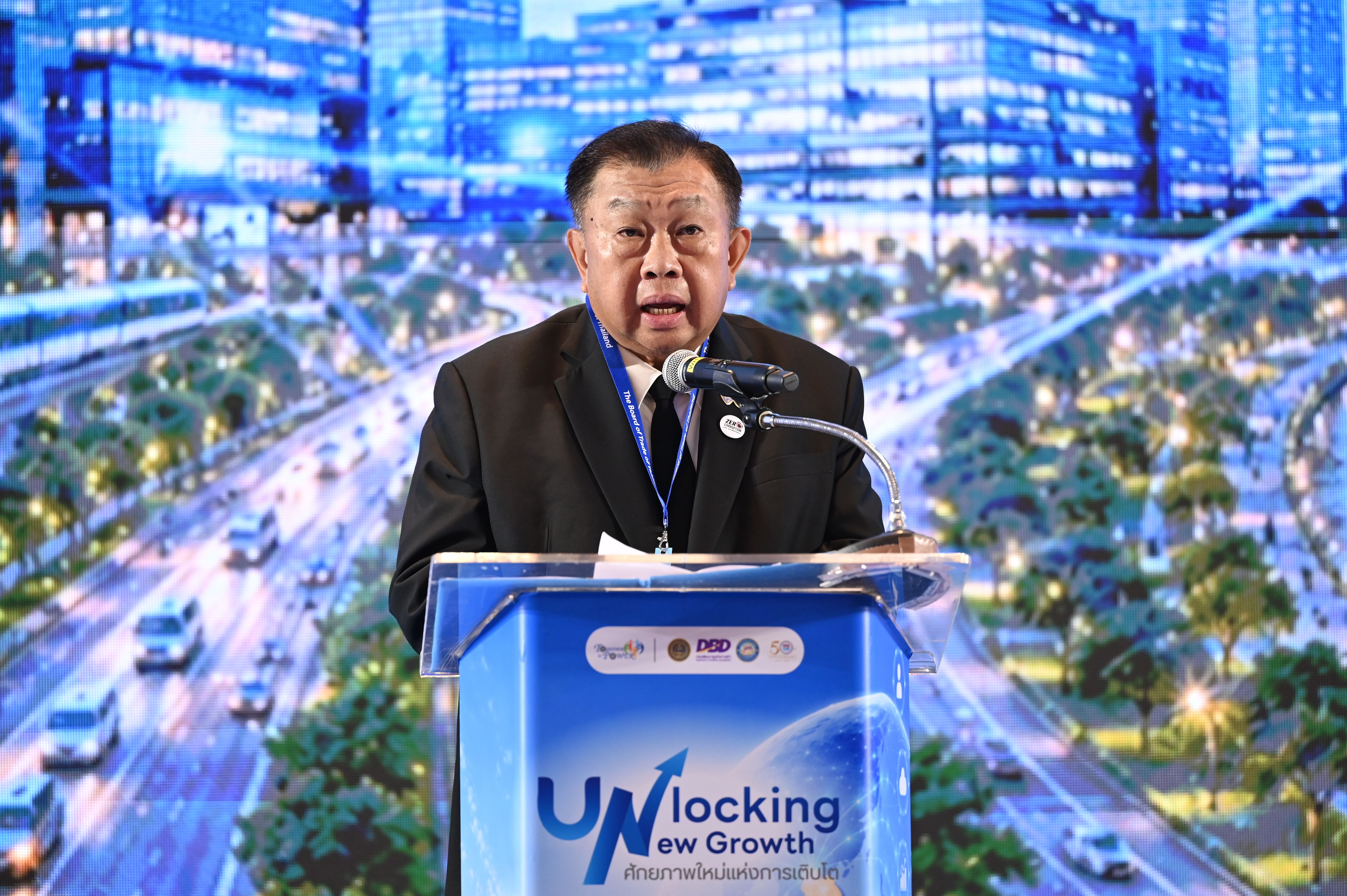 Man speaks at "Unlocking Growth" podium, backed by a futuristic digital city.
