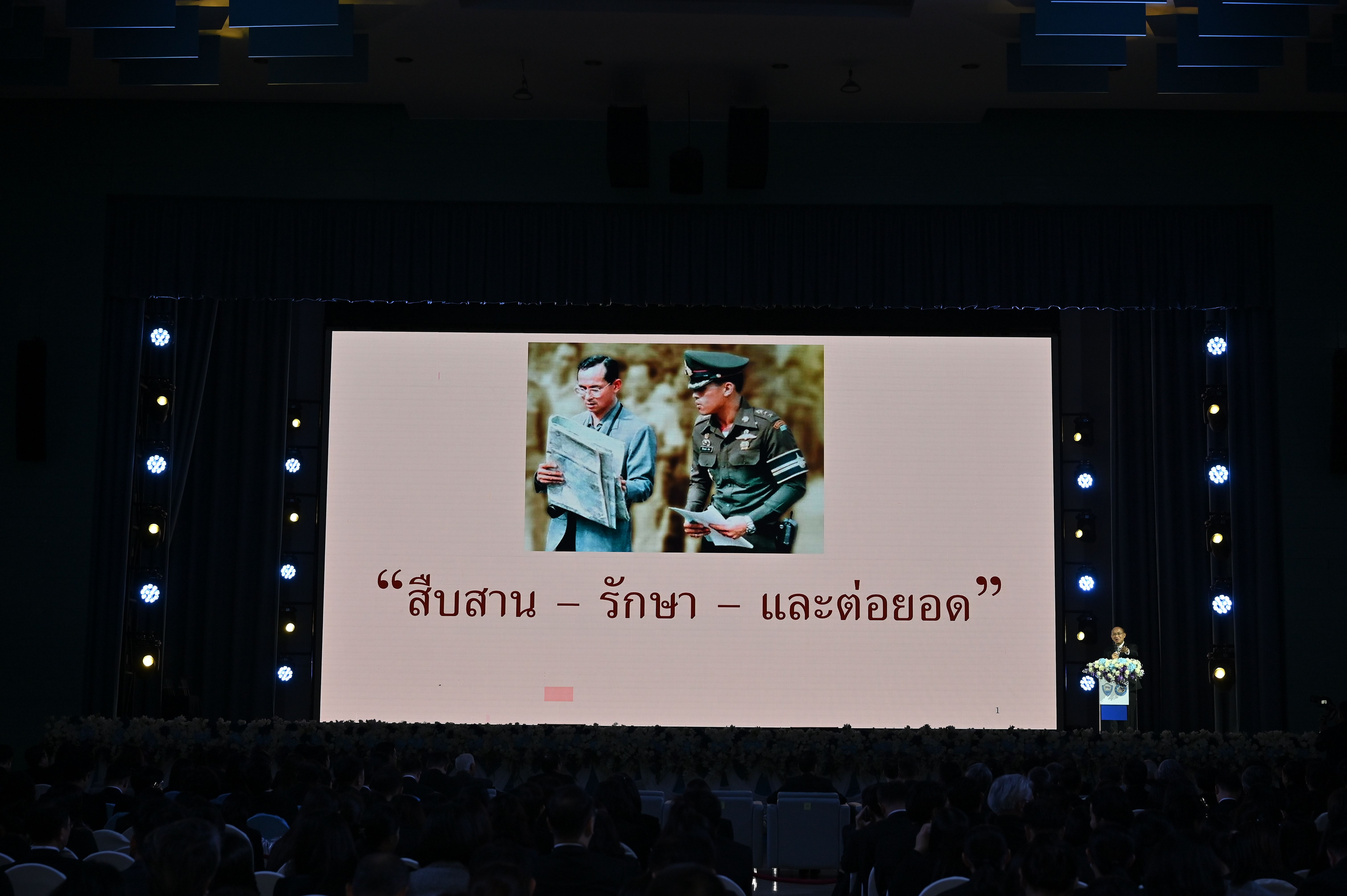 Large screen shows two men in uniforms and Thai text during a presentation.