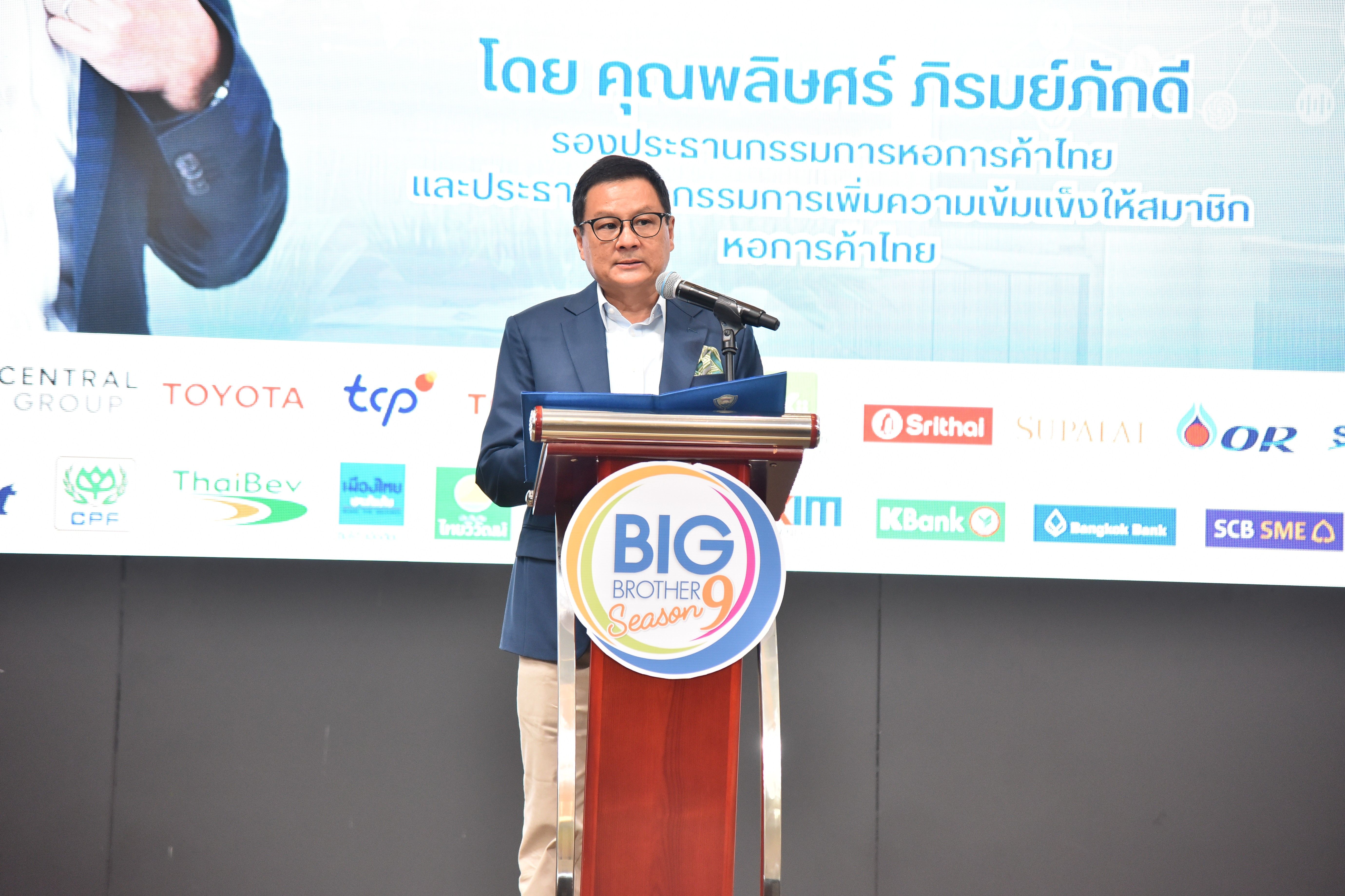 Man in suit speaking at a wooden podium with a 'BIG BIZ' logo at a conference.