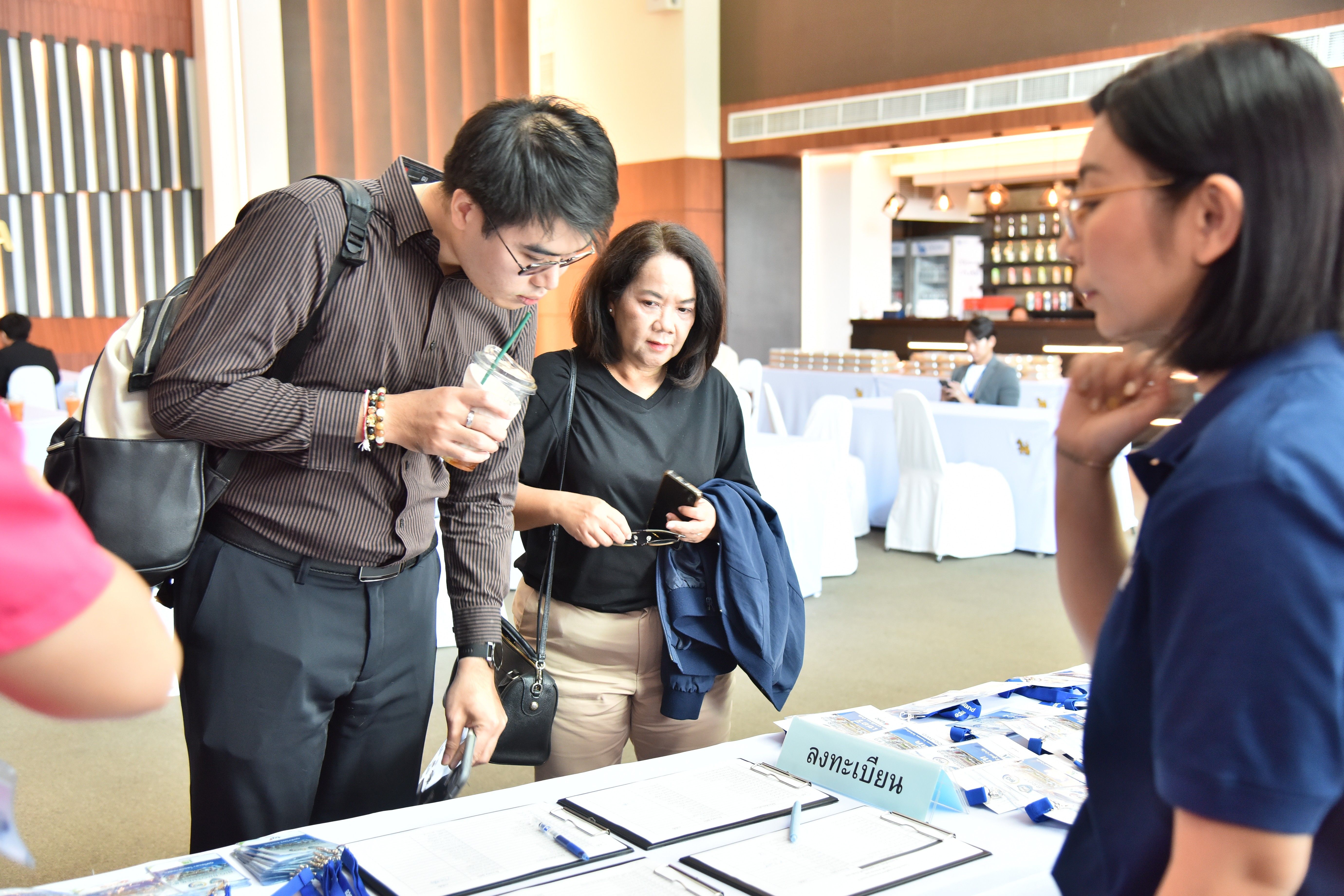 Conference attendees review documents on a table while a staff member provides information.