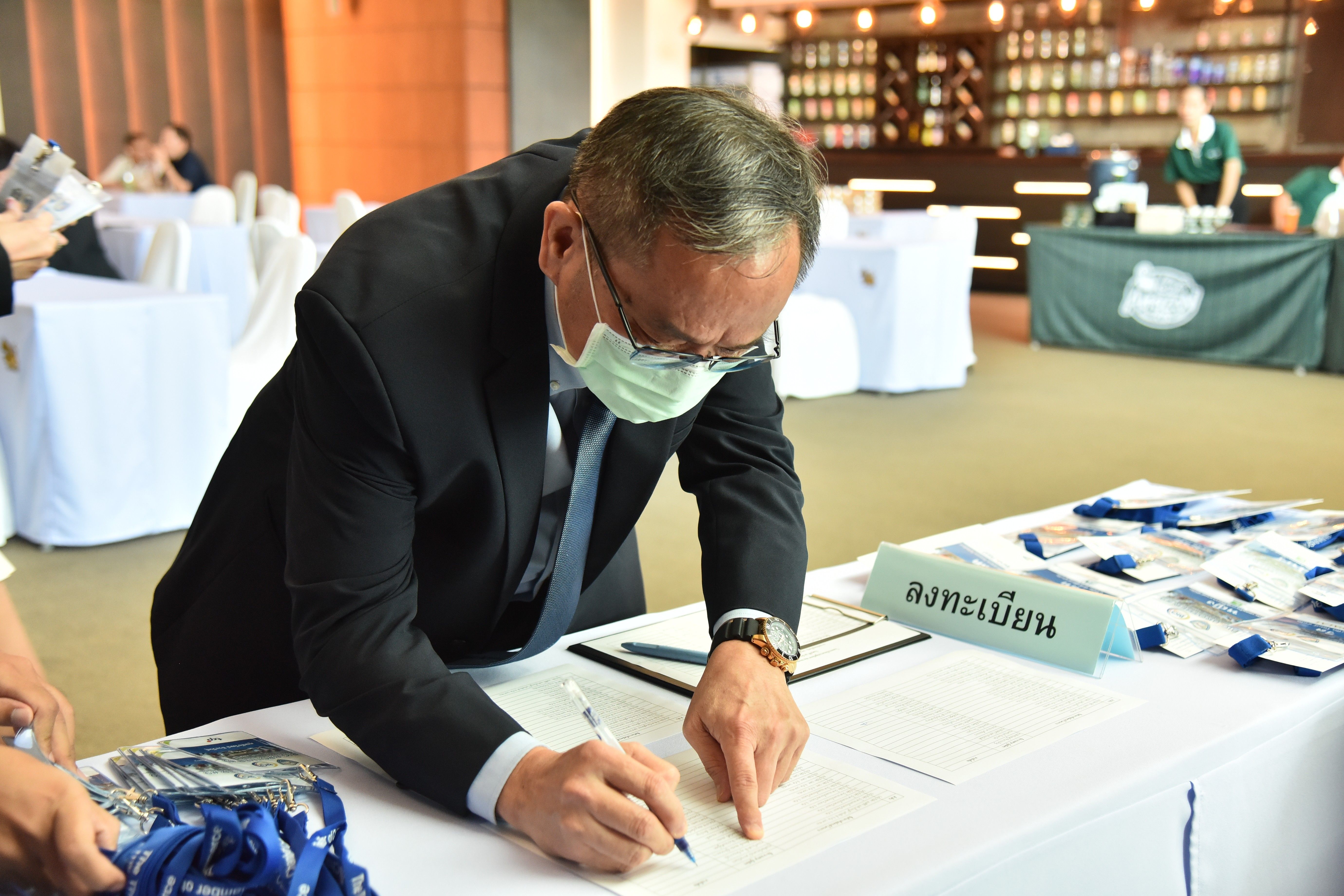 Man in suit and face mask signs a registration form at an event.