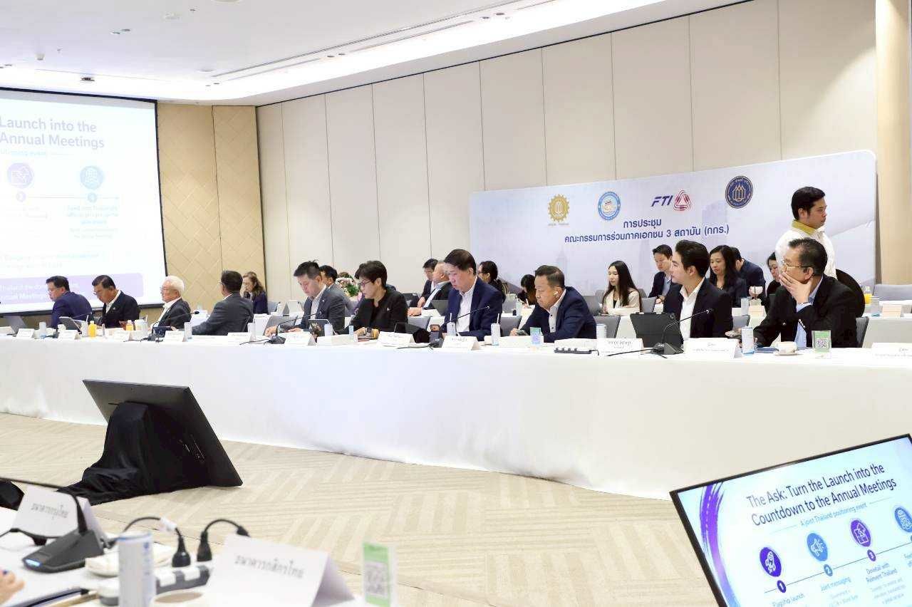 Professionals seated at a long table during a conference, with presentations displayed on screens.