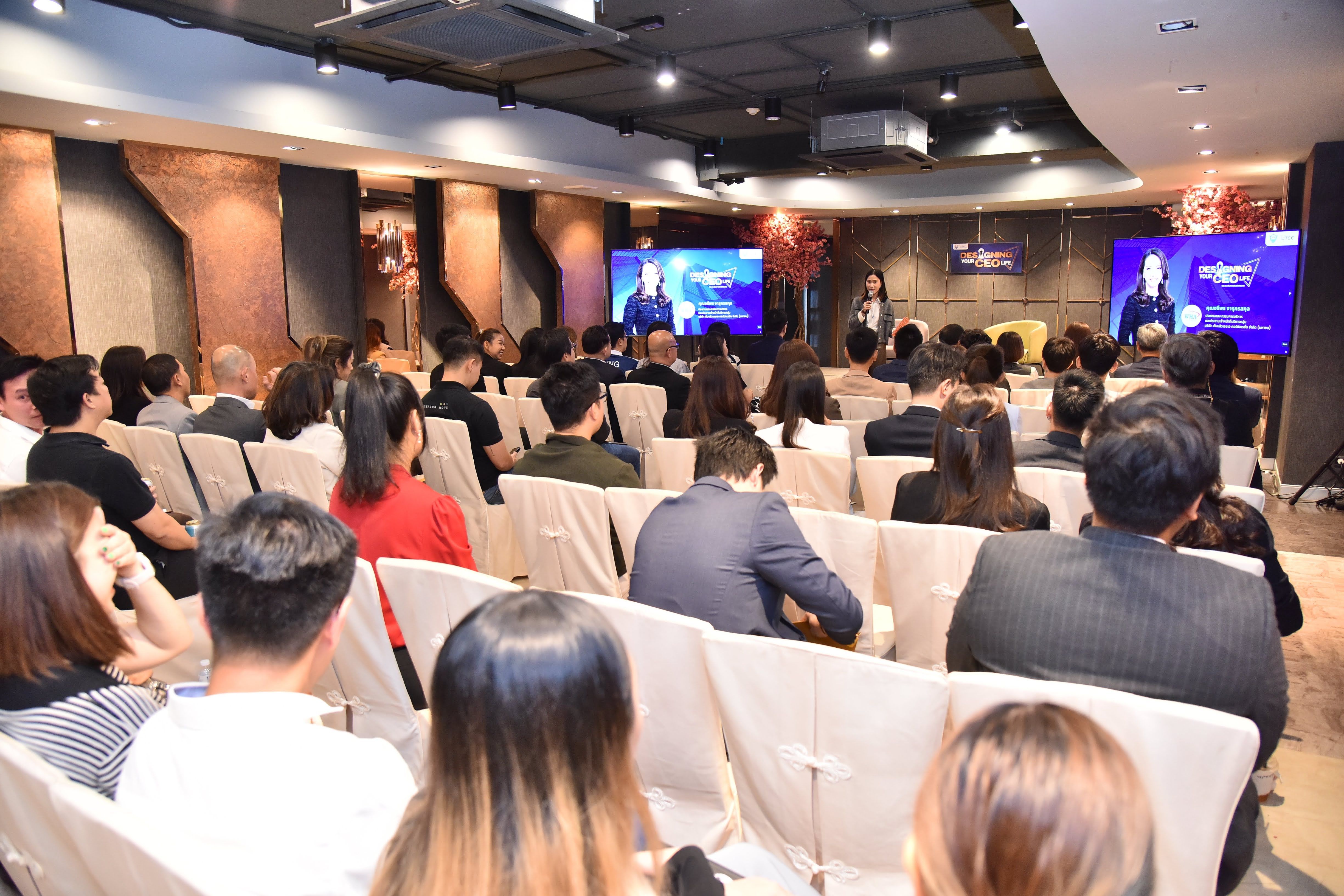 Audience in a conference room watching a speaker and two large presentation screens.
