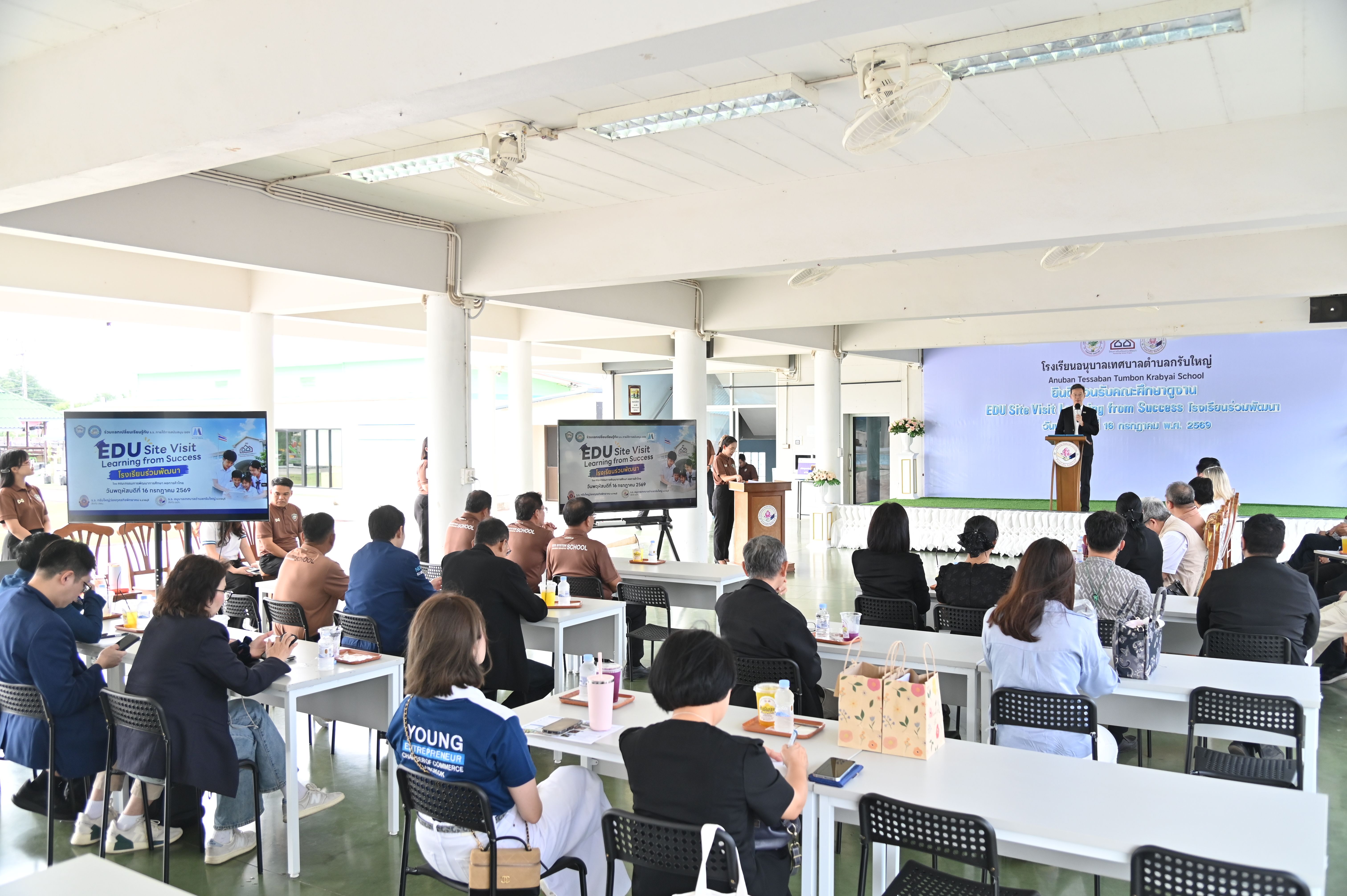Attendees listen to a speaker at a podium during an indoor presentation event.