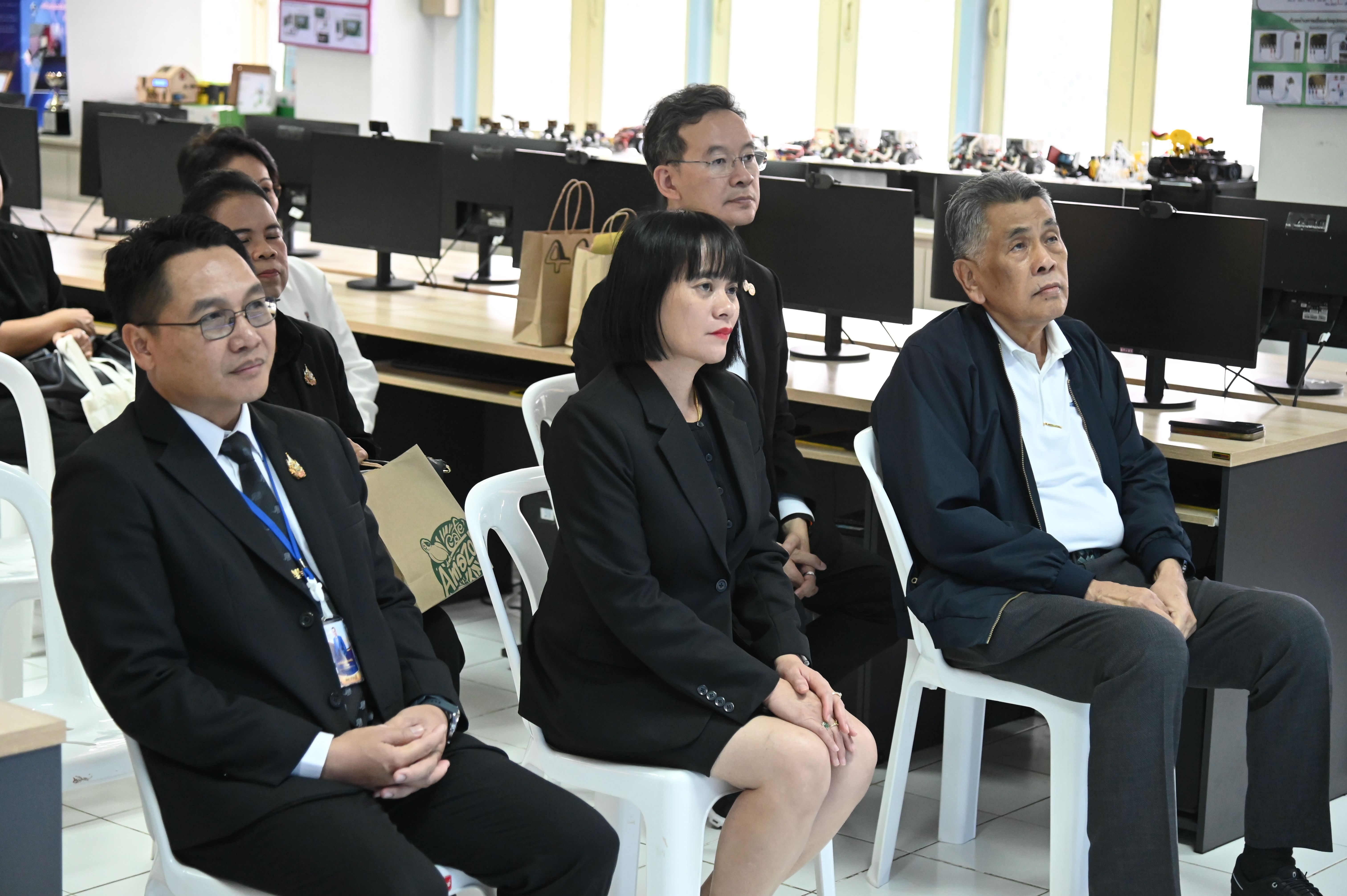 Three professionals in business attire sit attentively in a room with computer monitors.