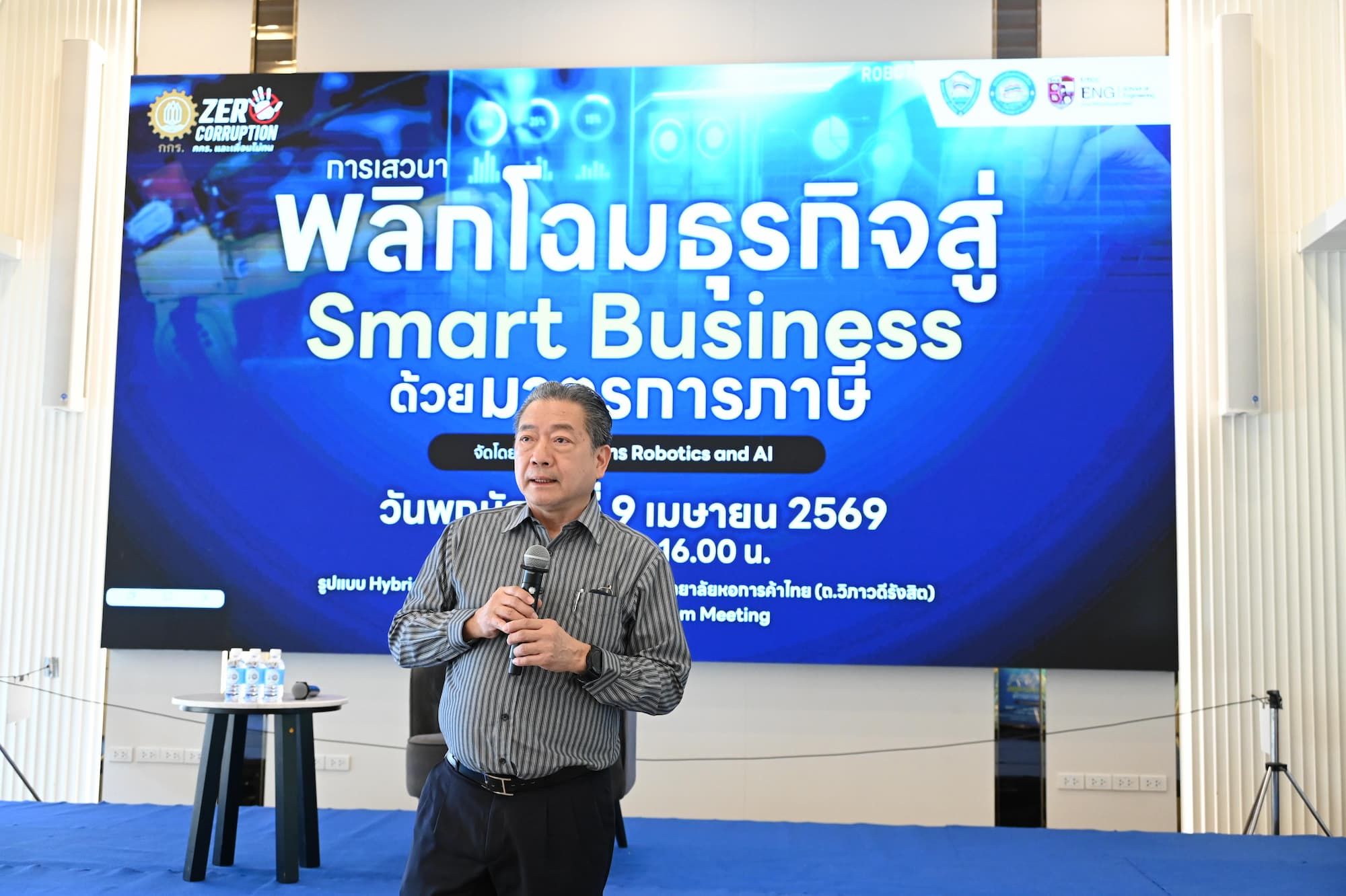 Man speaking into a microphone in front of a large screen displaying 'Smart Business'.